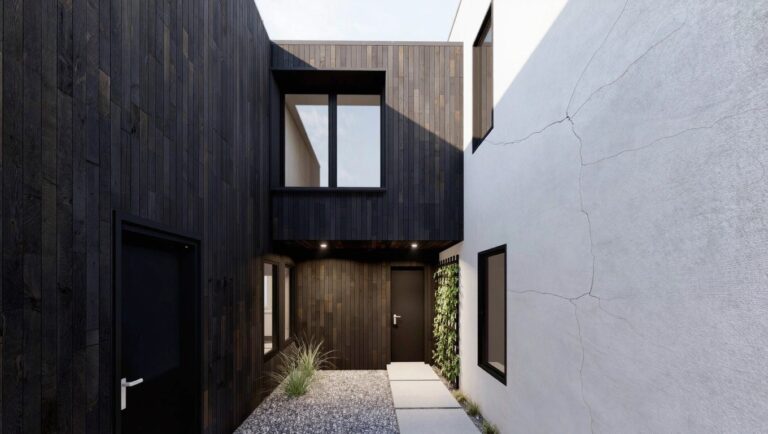 Modern small house exterior with black charred wood cladding on angled roof and walls, adjacent white rendered wall, large triangular window, black front door, gravel courtyard, concrete pathway, metal fence, and low plants.