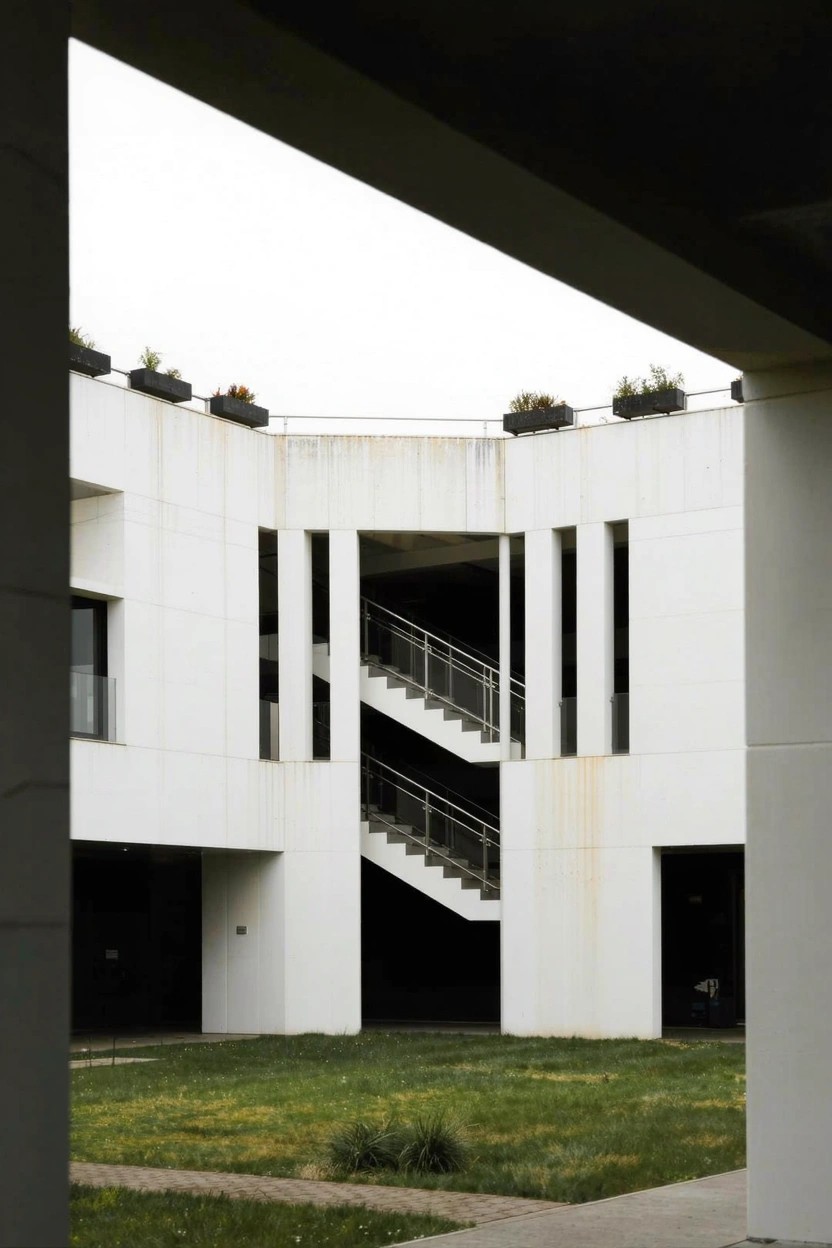 White modern building exterior with an enclosed courtyard containing multiple descending metal-railed staircases over grass, edged by elevated planters.