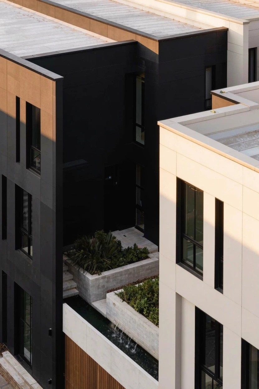 Aerial photo of modern multi-unit buildings featuring black paneled walls next to beige and white facades with a rectangular planter box containing greenery and a shallow water channel at the base.