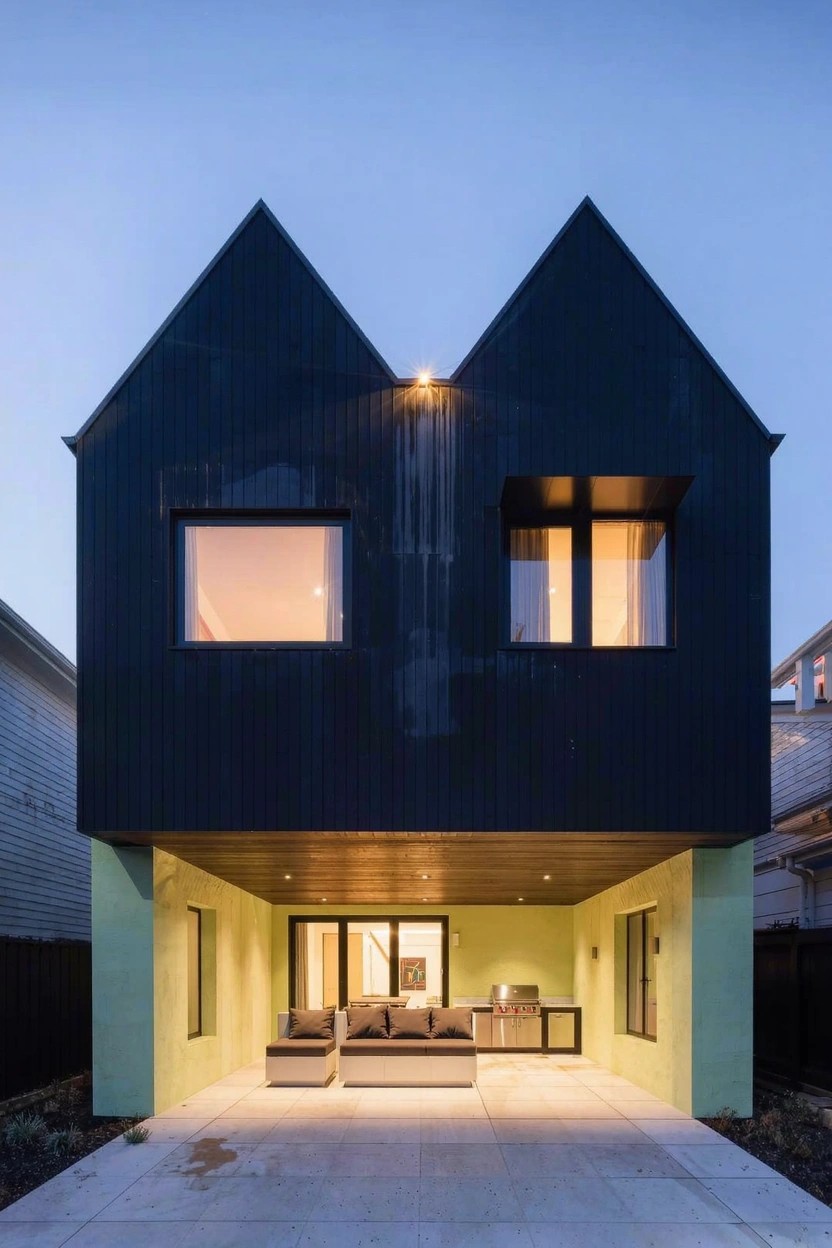 Black house with two gabled roofs elevated above a lime green base enclosing a lit patio and seating area at dusk.