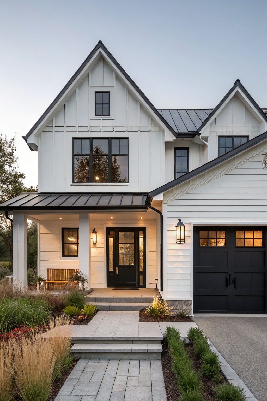 Two-story modern farmhouse exterior with white shiplap siding, black metal roof, black-framed windows, covered front porch with bench and lanterns, black entry door, attached black garage door, concrete steps, and low landscaping at dusk.