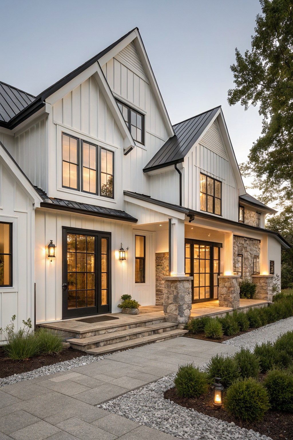 Modern farmhouse house exterior with white board-and-batten siding, black-framed grid windows, black metal roof, covered entry porch with stone pillars and glass doors, stone steps, and gravel-edged pathway with shrubs.