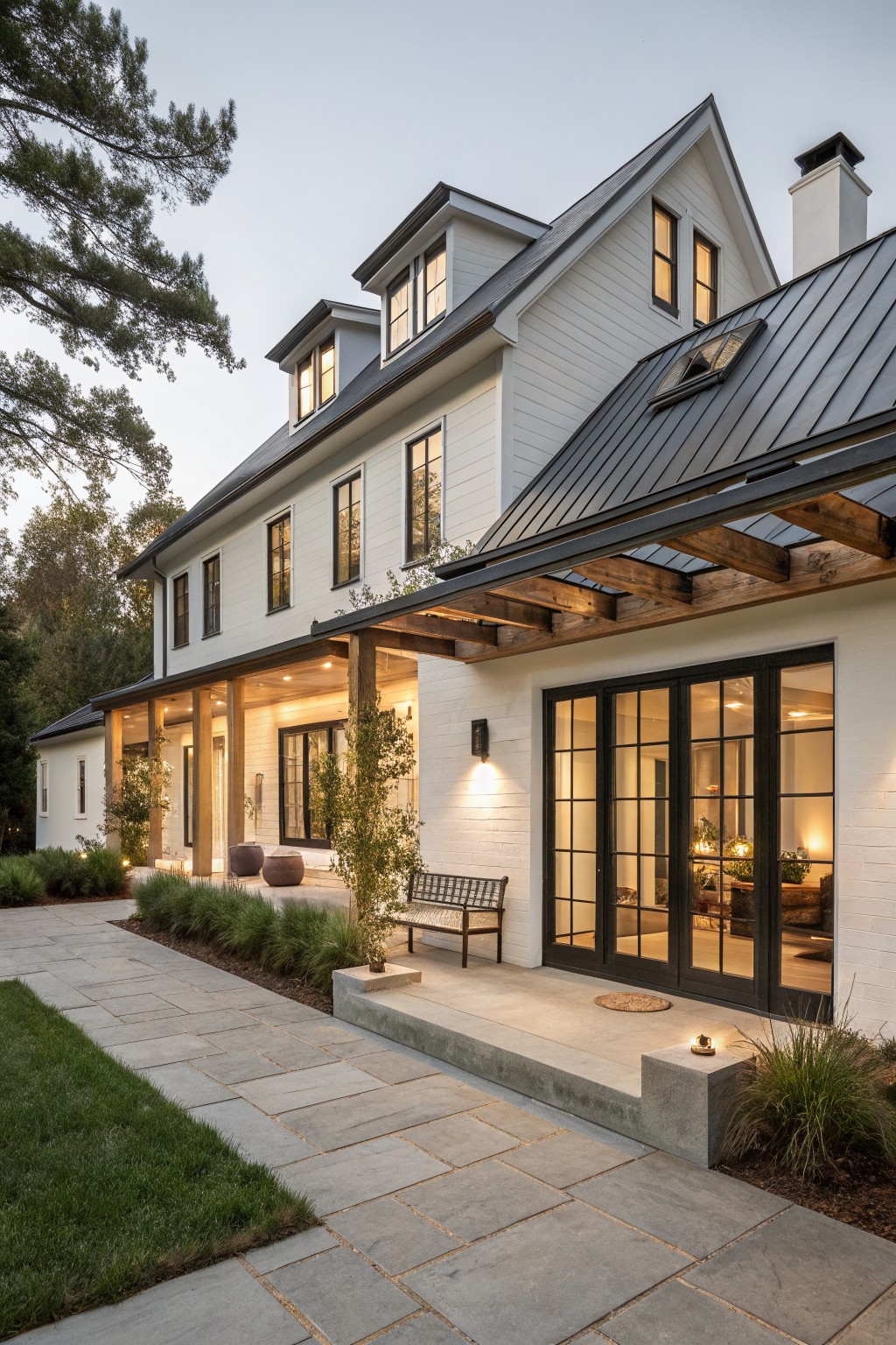 Two-story white modern farmhouse exterior with black-framed grid windows and doors, covered porch with wood beams, concrete steps, and potted plants along a stone path.