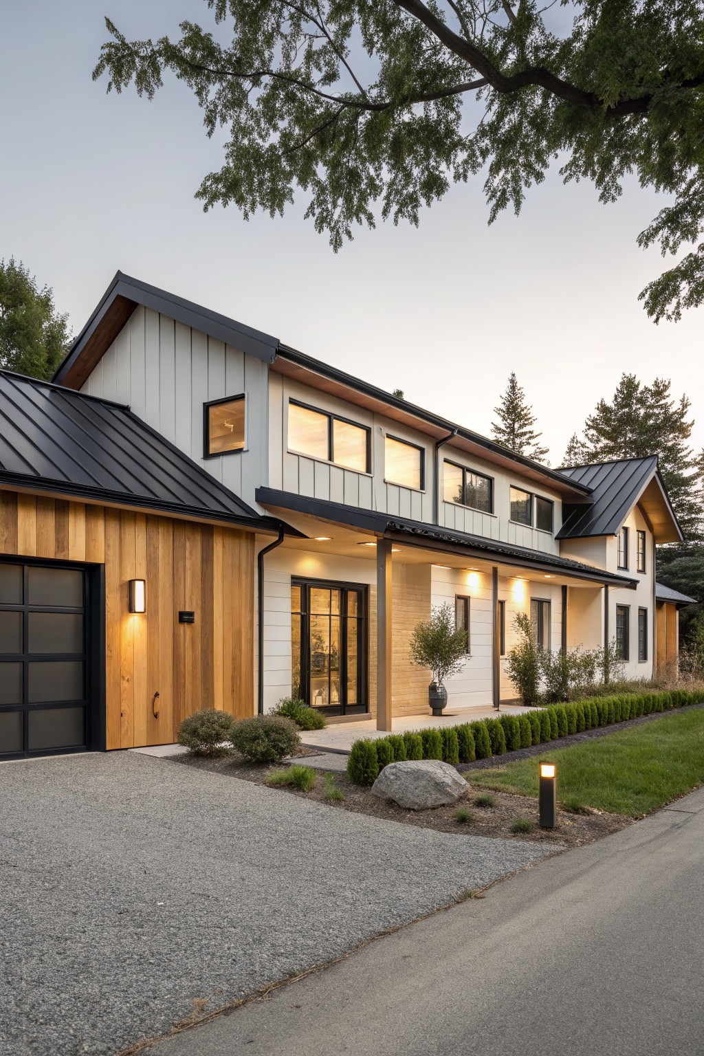 Two-story modern farmhouse exterior with white horizontal siding, vertical wood siding and glass garage door on the left, black metal roof, covered porch with slim supports, gravel driveway, boxwood hedges, and trees in the background.