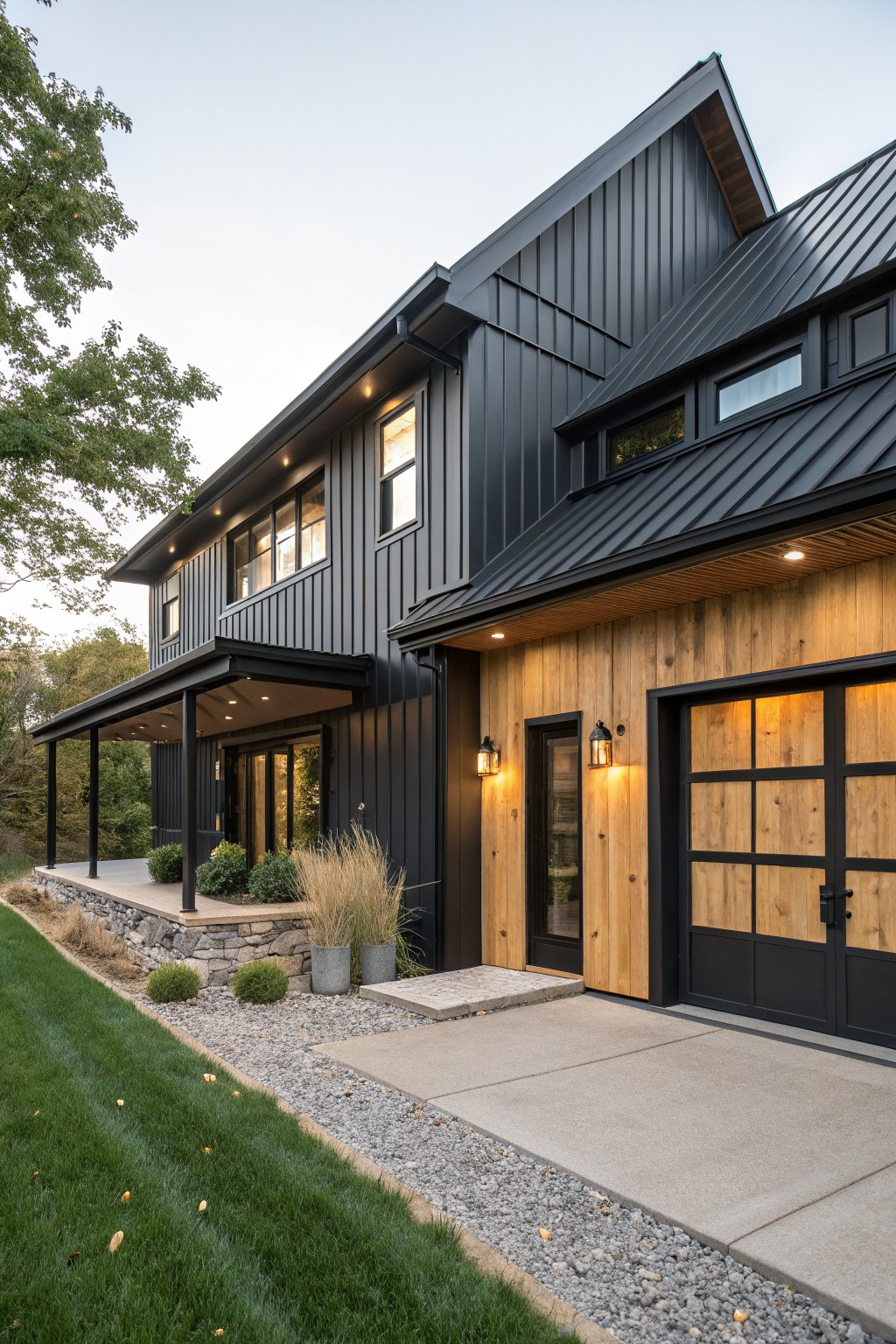 Two-story house exterior featuring black vertical siding, black metal roof, natural wood garage door and accents, covered porch, stone retaining wall, and lawn with gravel path.