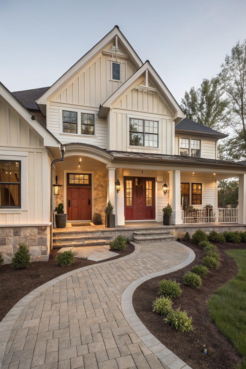 Two-story modern farmhouse exterior featuring cream shiplap siding, black roof and trim, red double front doors under a covered porch with lanterns, stone foundation accents, and a curved brick pathway with shrubs leading to the entry.
