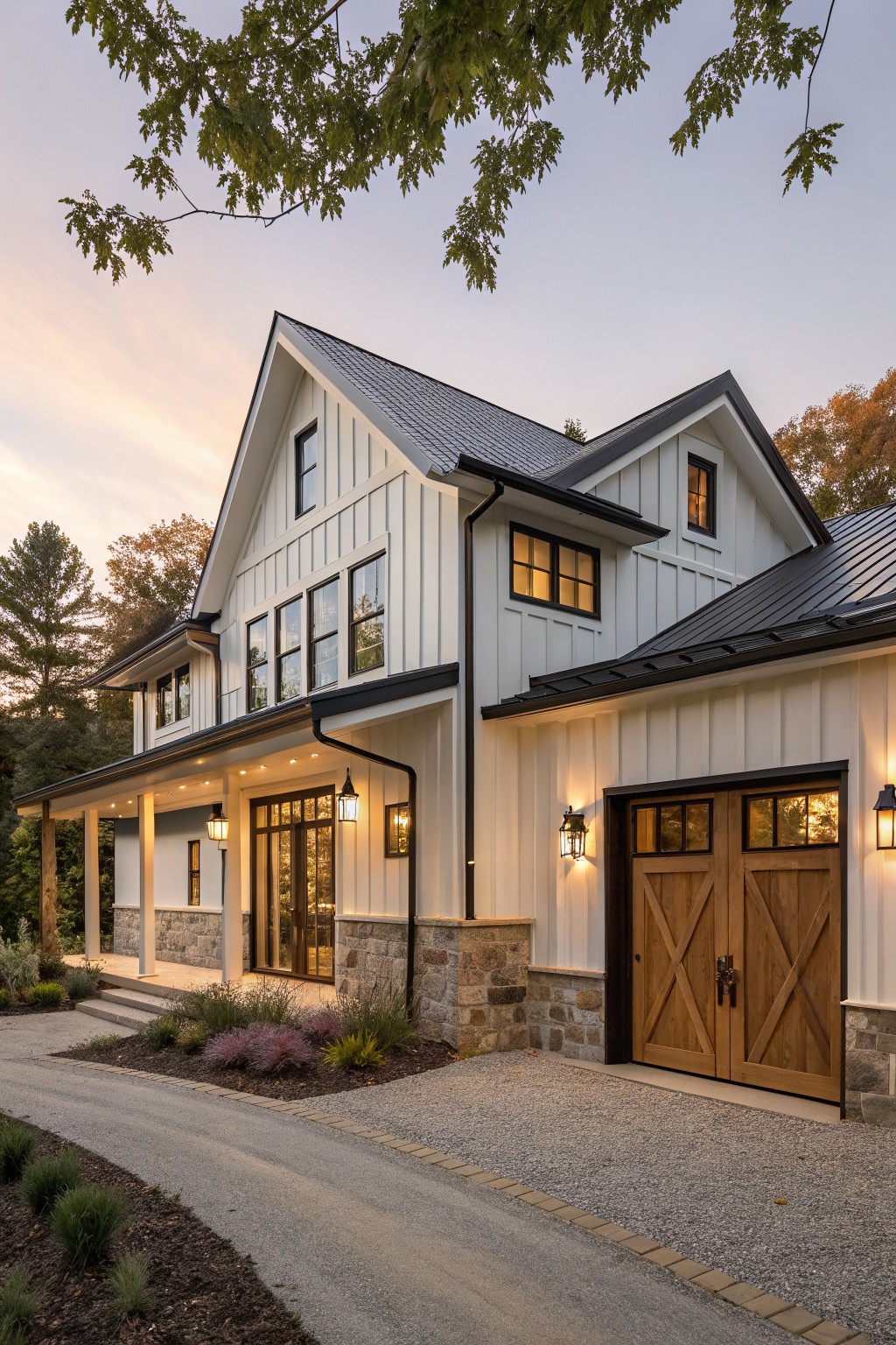 White board-and-batten modern farmhouse with black metal roof, dark wood X-pattern garage doors, covered porch, stone accents, and gravel driveway surrounded by landscaping at dusk.