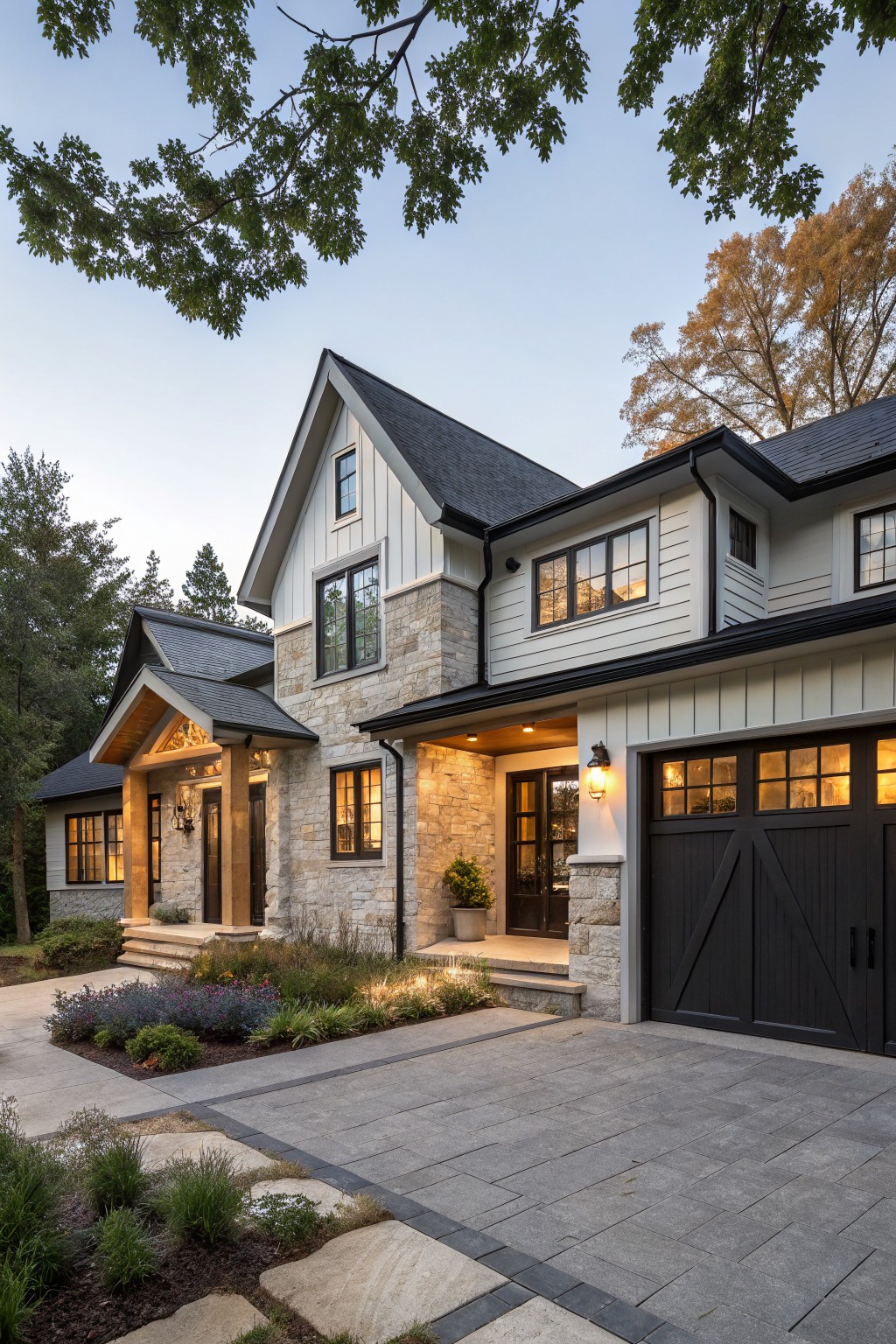Two-story modern farmhouse exterior with white board-and-batten siding, beige stone accents around entry and garage, black shingle roof and garage doors, wooden porch supports, front landscaping beds, and gray paver driveway.