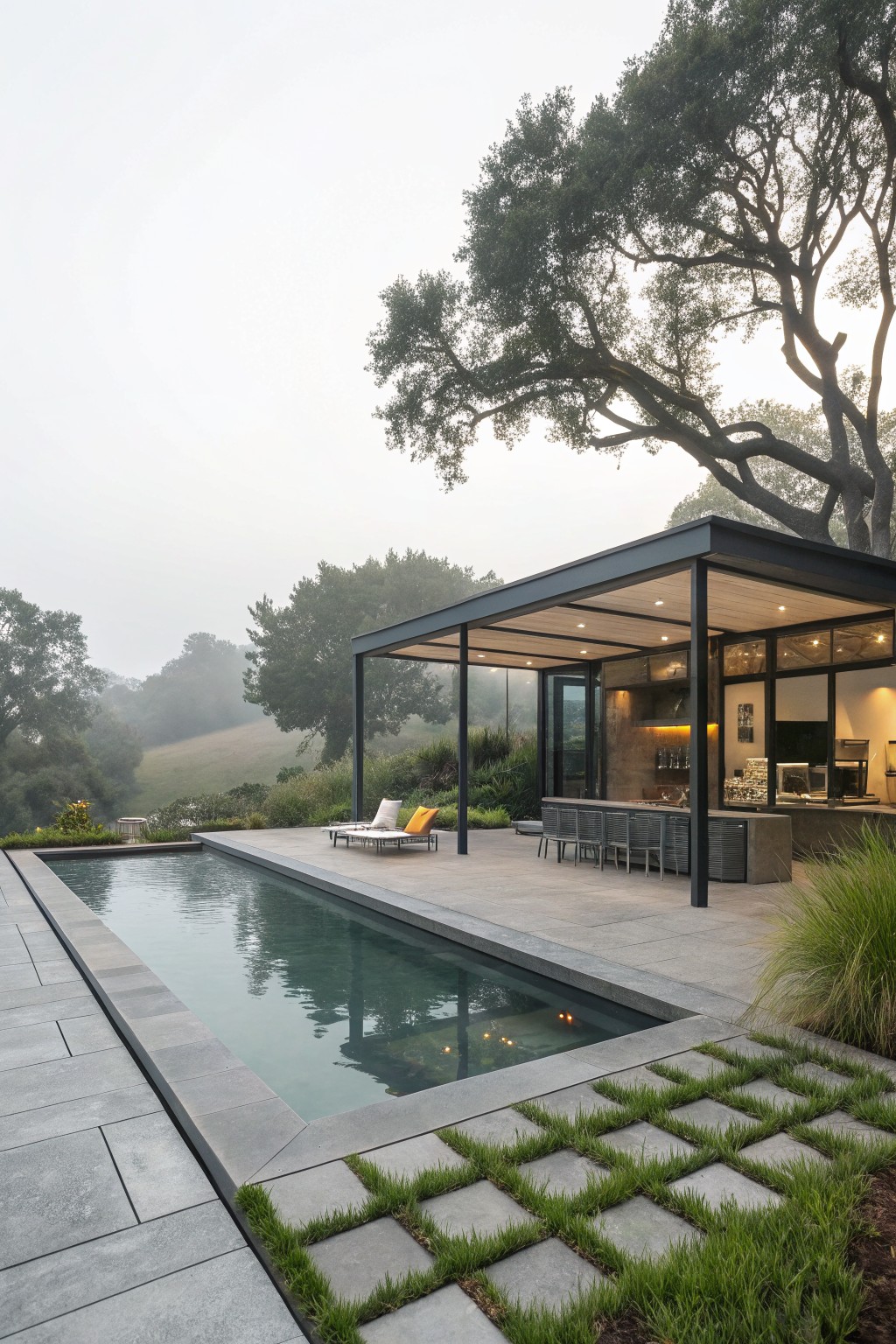 Modern poolside patio with sleek cabana, lounge chairs, and misty hillside view.