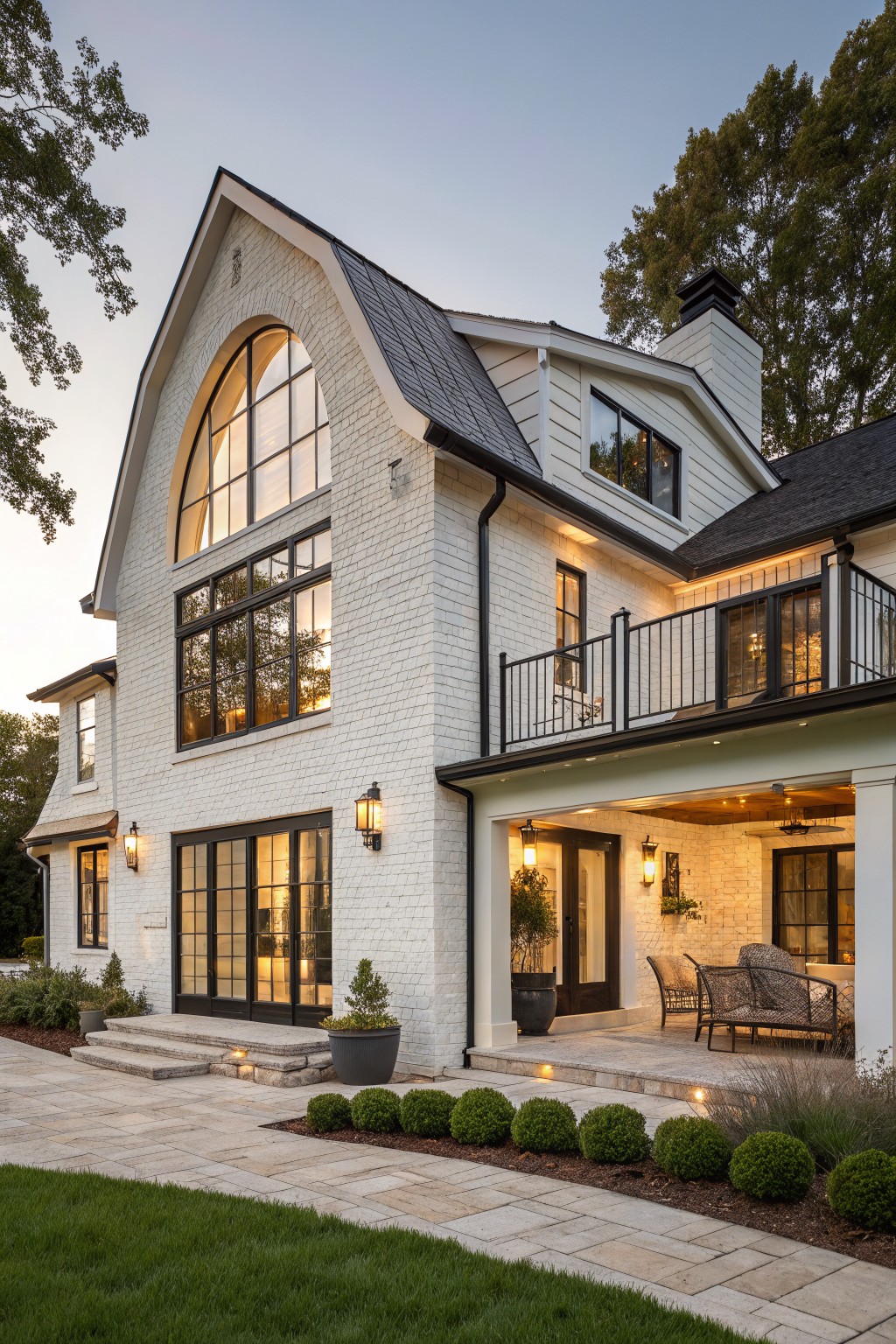 Elegant white brick house with large arched window and black balcony at dusk.