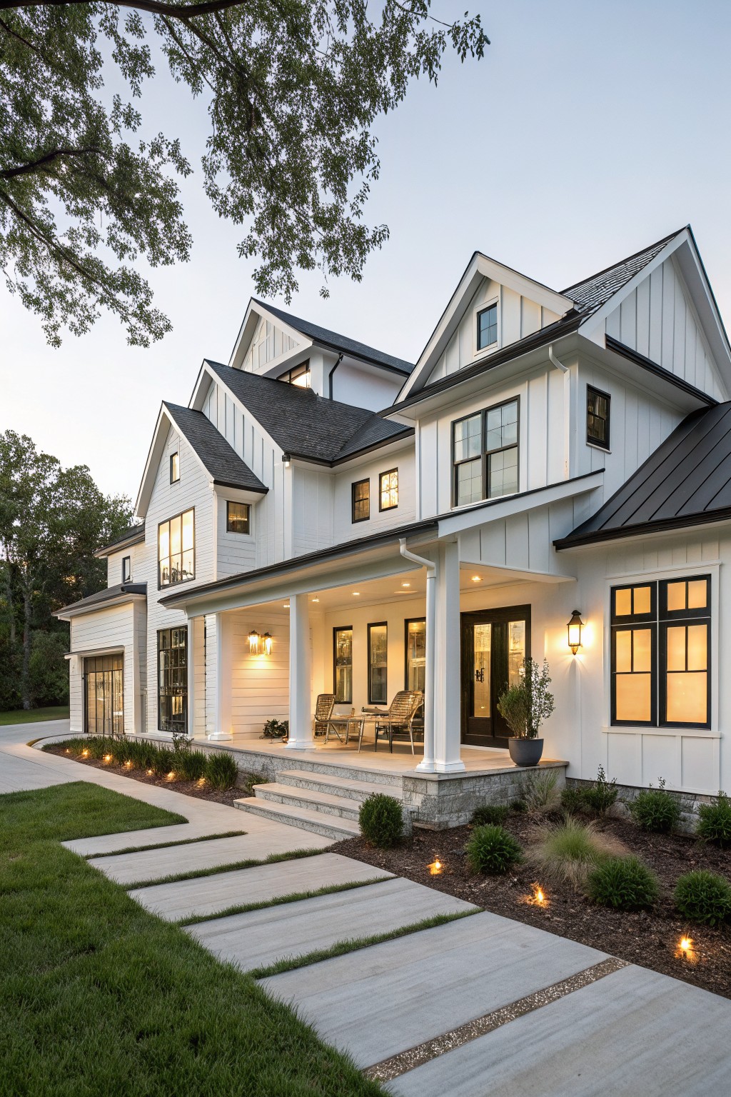 Two-story modern farmhouse exterior with white board-and-batten siding, black metal roof, gabled peaks, wraparound porch with columns, large windows, and landscaped pathway at dusk.