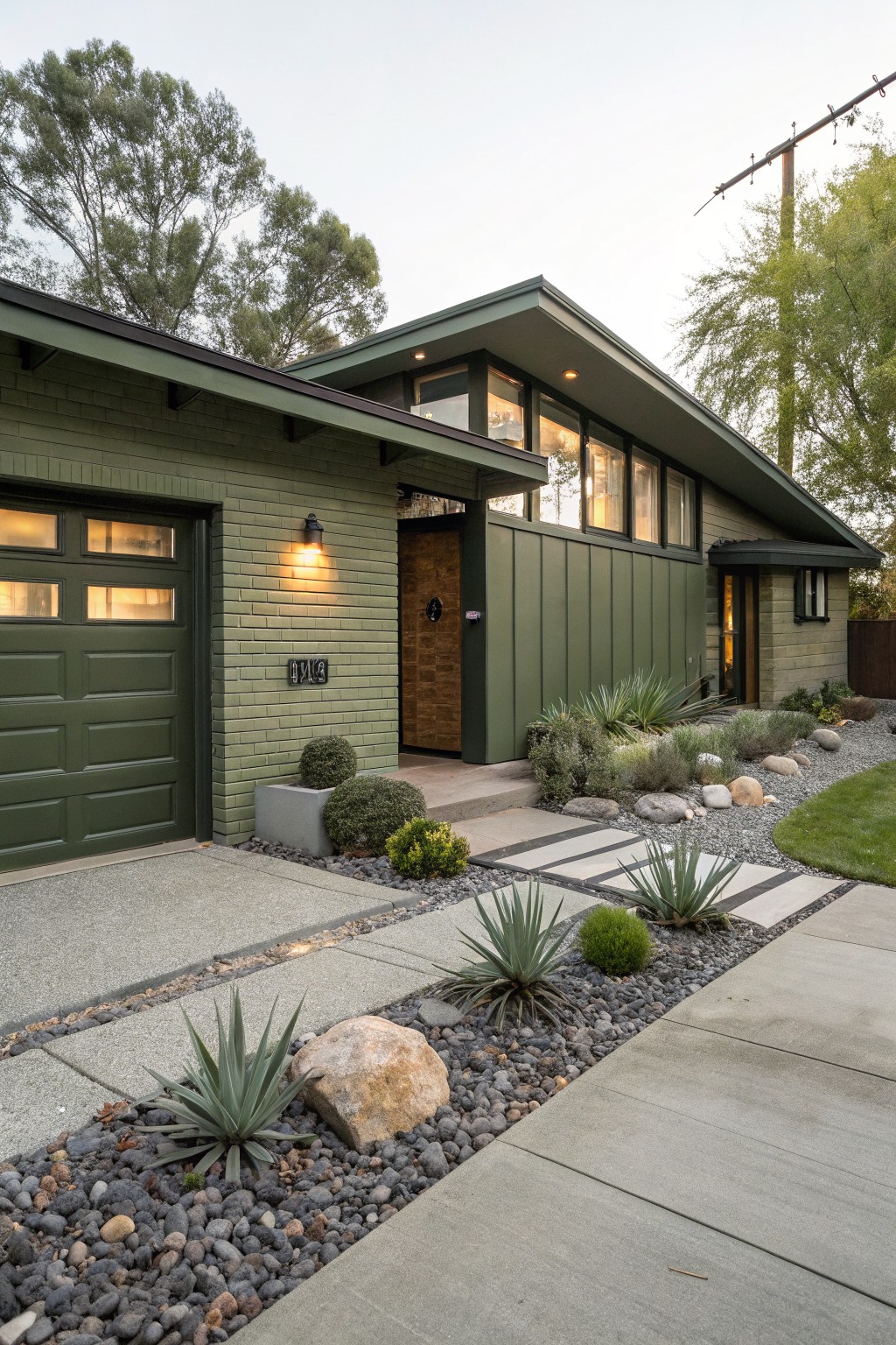 Green painted brick garage and vertical siding house exterior with cantilevered roof, large windows, wood entry door, and succulent landscaping along concrete walkway.