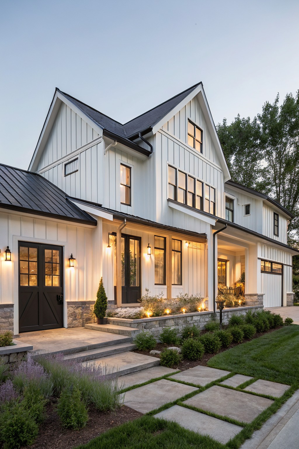 A two-story modern farmhouse house exterior featuring white board-and-batten siding, black standing-seam metal roof, black double front doors, covered porch with lanterns, garage, steps, and low landscaping at dusk.