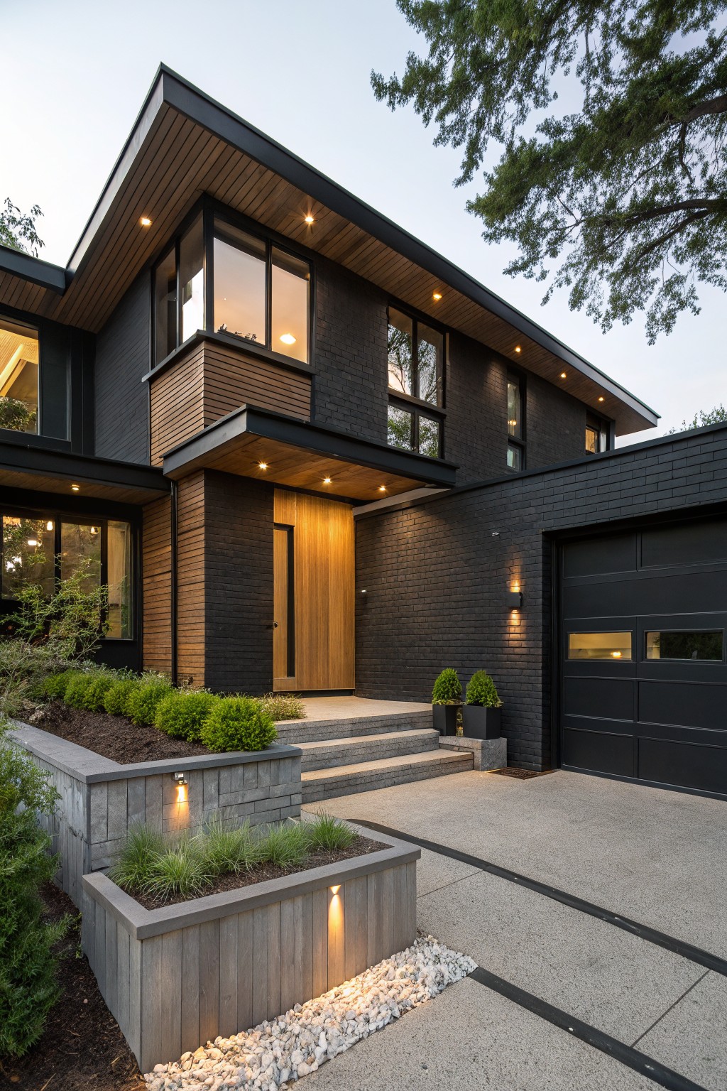 Two-story modern house with black brick exterior, horizontal wood cladding on upper sections and entry overhang, large windows, wood front door, black garage door, steps to entry, low plantings, and gravel path at dusk.