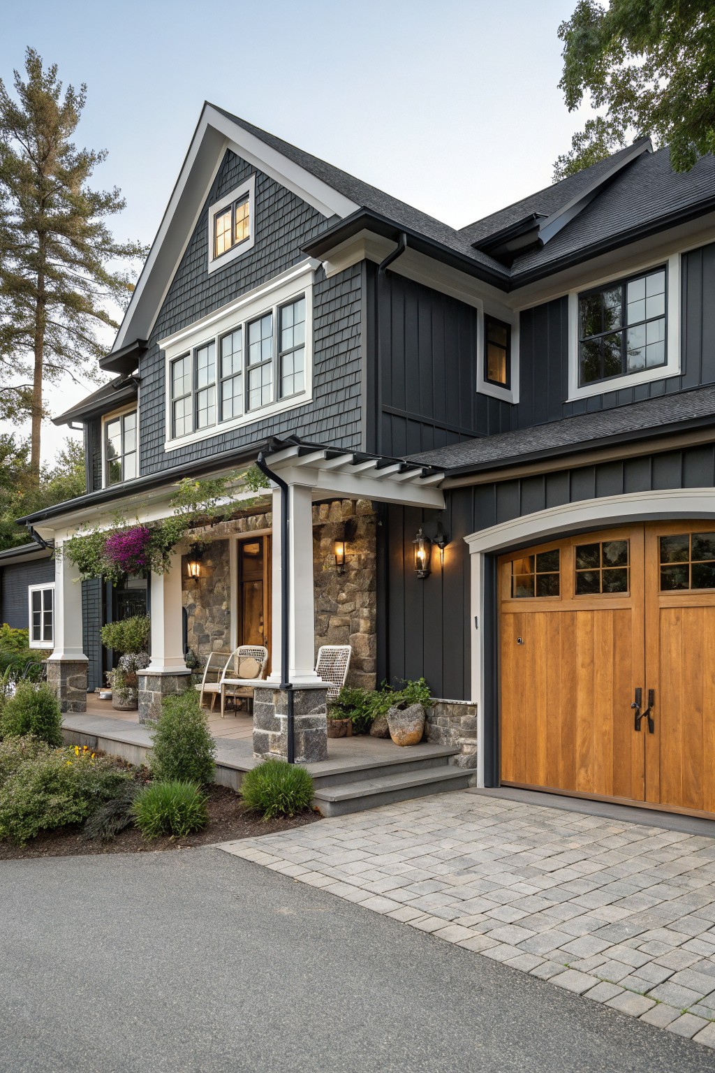 Modern two-story dark gray house with stone porch, wooden garage doors, and paved driveway.