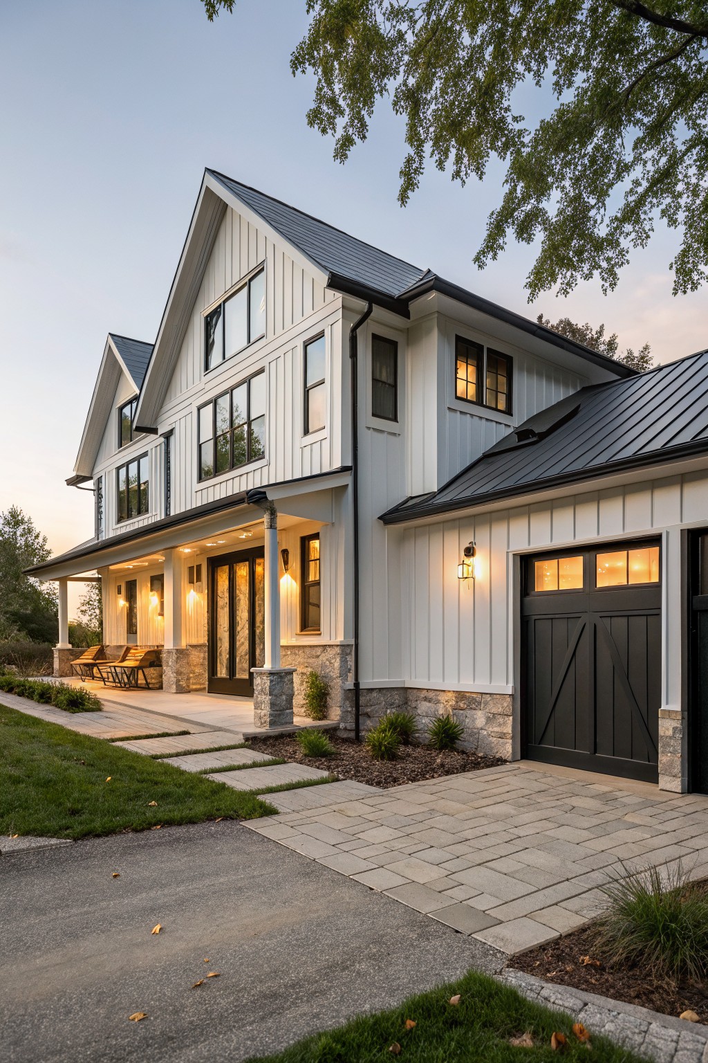 Two-story modern farmhouse house with white board-and-batten siding, black-framed windows, covered front porch, attached garage with black door, stone accents, metal roof, pathway, landscaping, and trees at dusk.