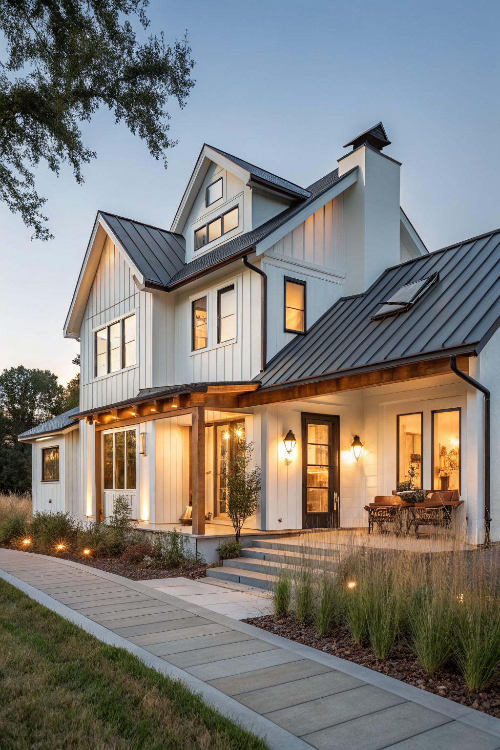 White board-and-batten modern farmhouse with dark standing seam metal gabled roof, covered front porch, pathway, and landscaping at dusk.