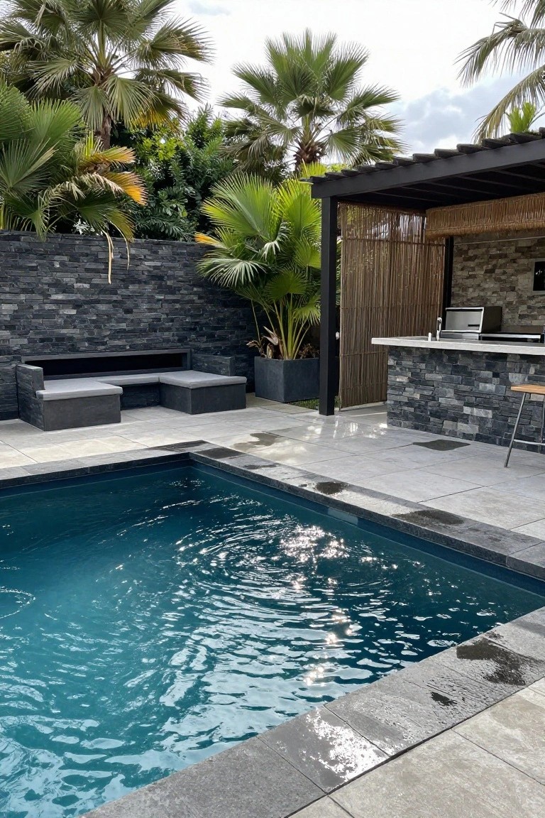 Outdoor pool with dark slate stone walls, built-in gray lounge seating, black metal pergola with bamboo screens over a stone-accented bar kitchen, surrounded by palm trees and potted plants on a tiled patio.