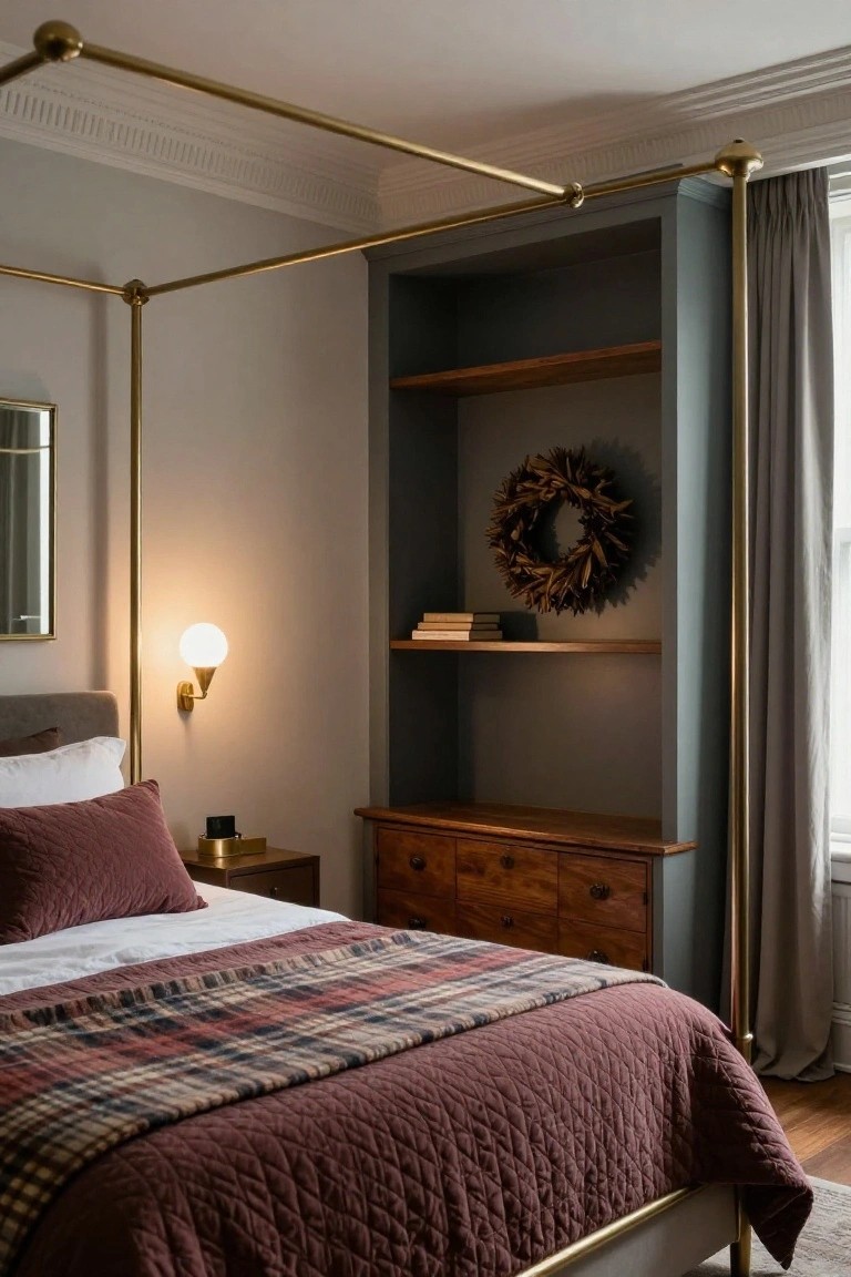 Brass four-poster bed with white sheets topped by deep red quilted bedspread and plaid throw, beside wooden nightstand with lamp, in bedroom with built-in gray shelves holding wheat wreath and books, gray curtains at window.
