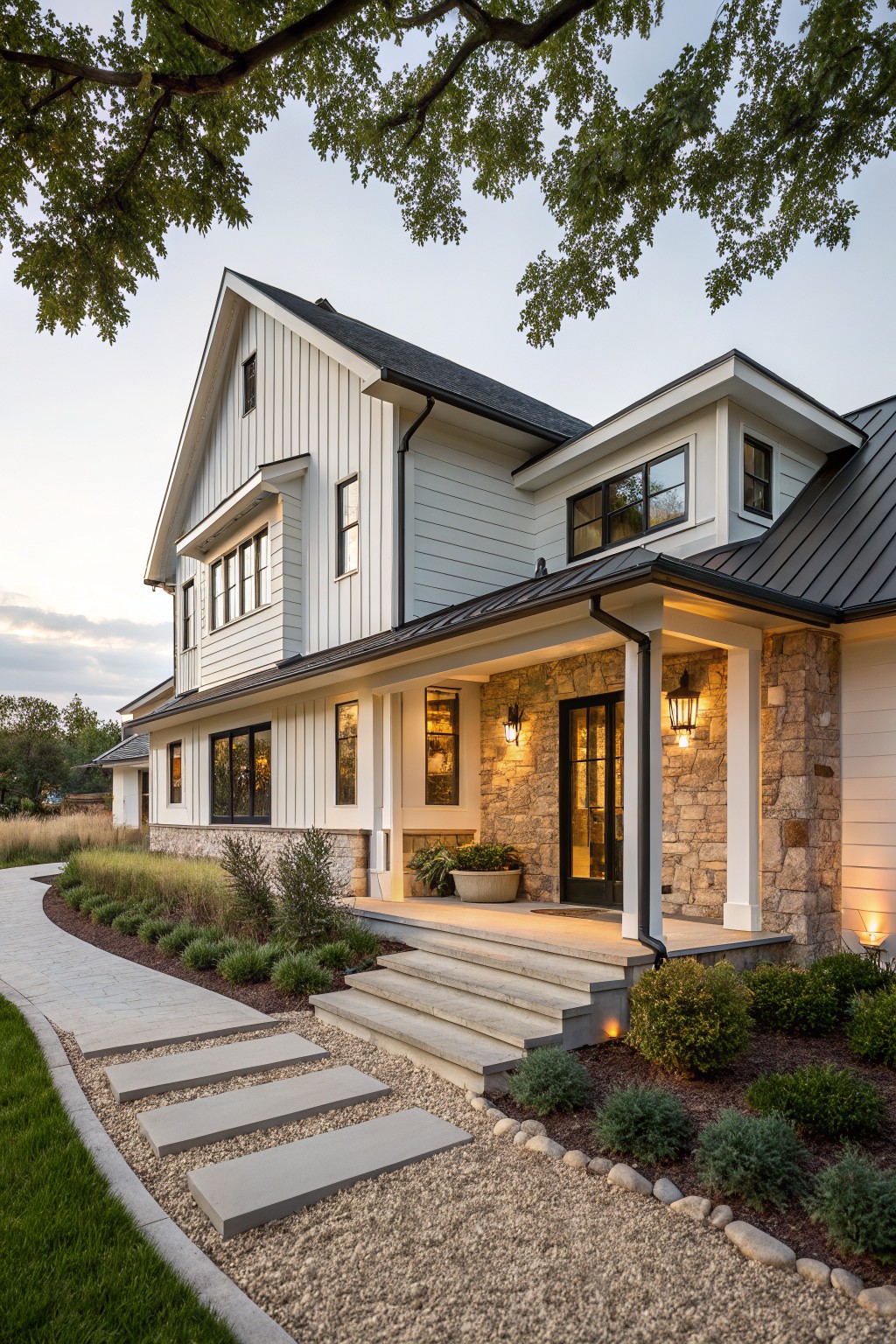 Two-story modern farmhouse exterior with white board-and-batten siding, black metal roof, stone veneer on porch columns and base, covered entry porch, and landscaped path with steps leading to the door.