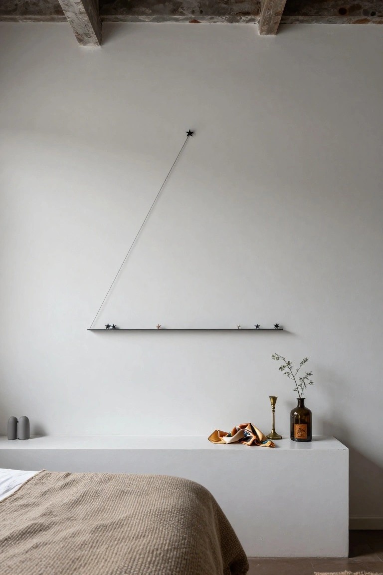 White-walled bedroom corner featuring a black floating shelf with small black star ornaments connected by a thin diagonal wire forming a triangular outline, next to a low white platform with bed, beige throw, gray candles, orange fabric, brass candlestick, and brown glass bottle on wooden beams ceiling.