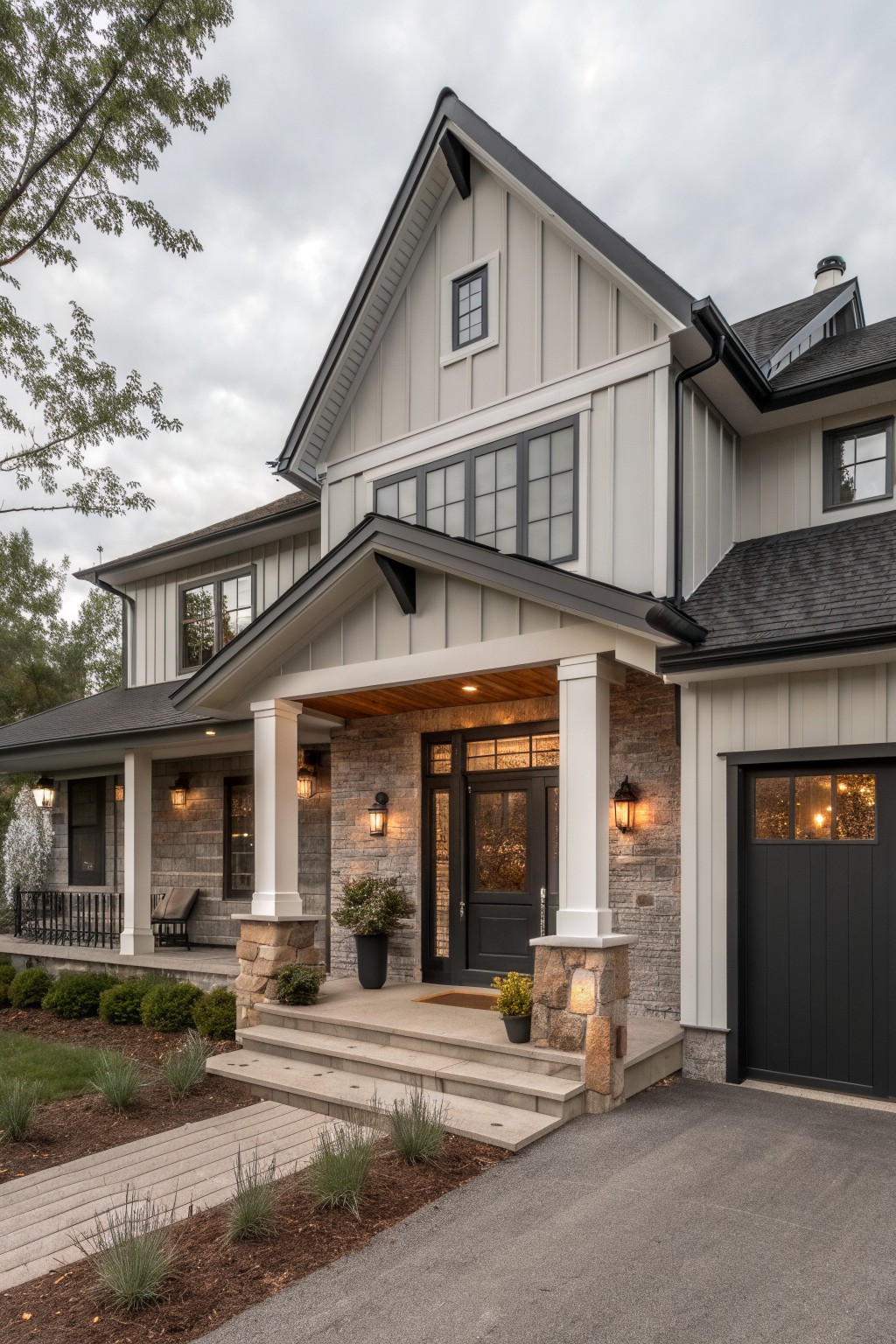 A modern farmhouse house exterior with light gray vertical siding, black shingle roof and trim, black-framed windows and garage door, covered front porch with white columns and stone base, landscaping, and concrete driveway.