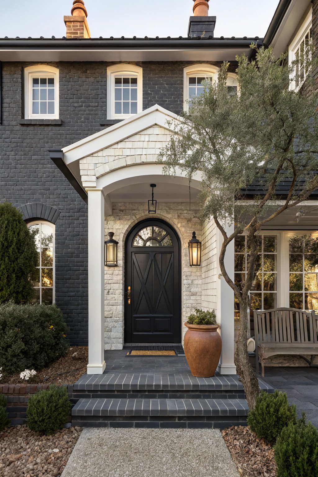 Elegant black-brick house with arched doorway and terracotta pot.
