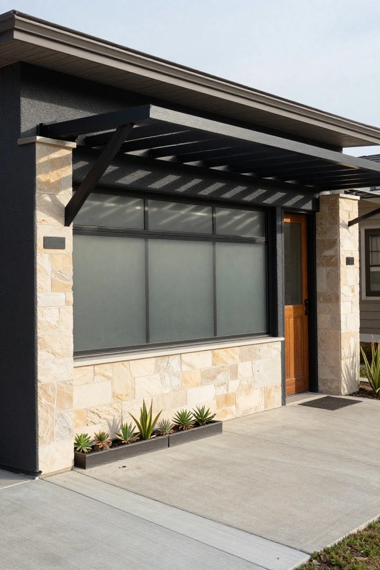 Modern house exterior with dark gray siding, beige stone-clad pillars flanking a wooden entry door and large frosted glass windows under a black metal pergola, concrete path, and potted agave plants.