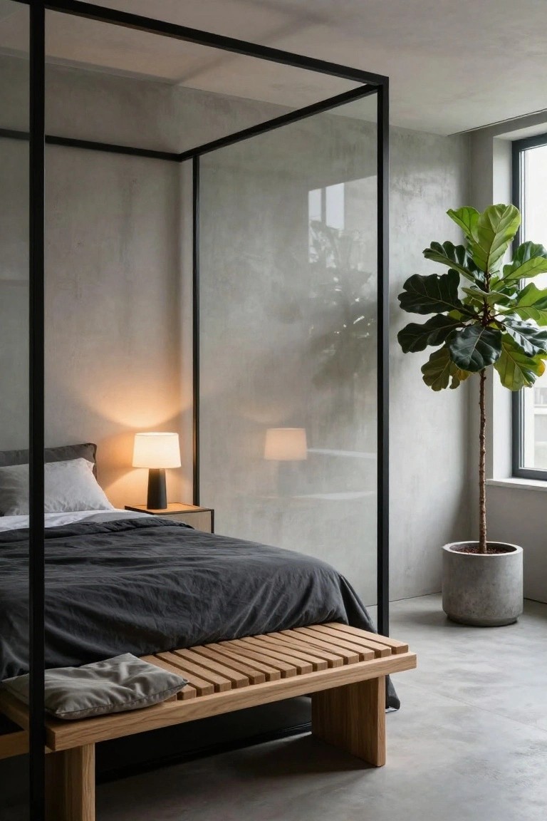 Bedroom with bed enclosed by black metal frame against concrete wall, oak slat bench at foot, bedside lamp on wood table, and fiddle leaf fig plant in concrete pot.
