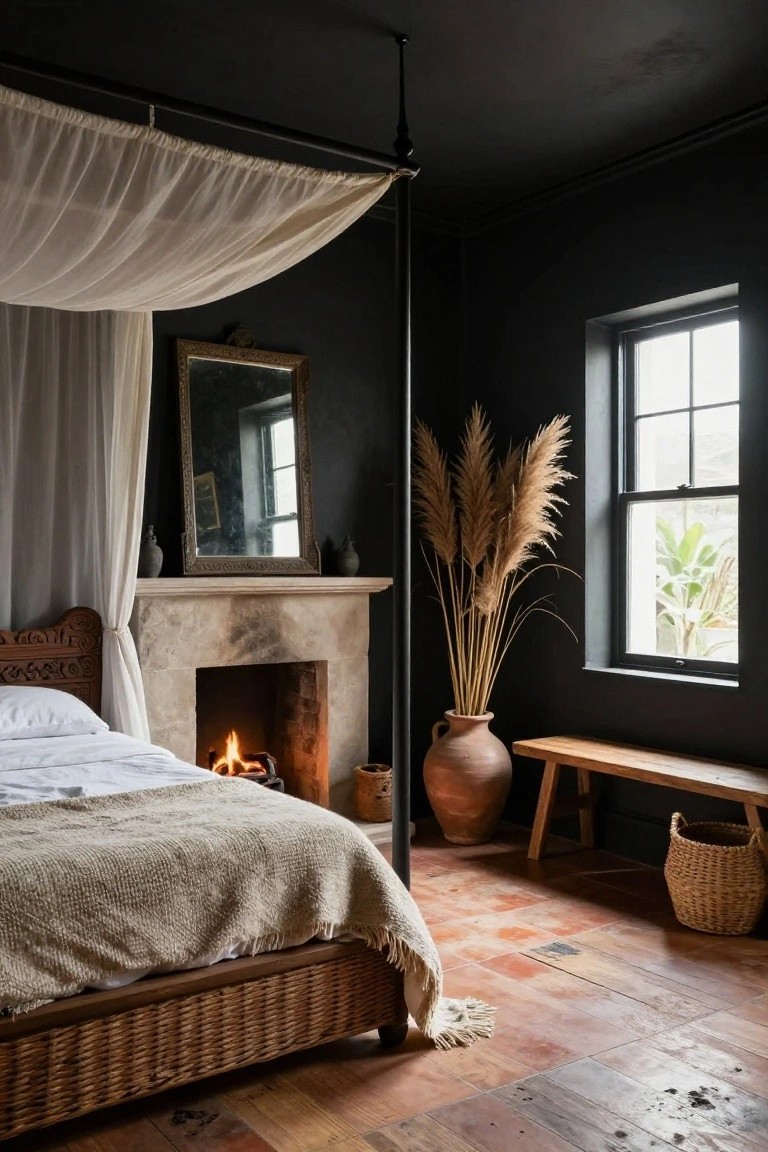 Dark-painted bedroom with rattan four-poster bed under white sheer canopy, stone fireplace with fire, pampas grass in terracotta pot, antique mirror, and window with plant outside.