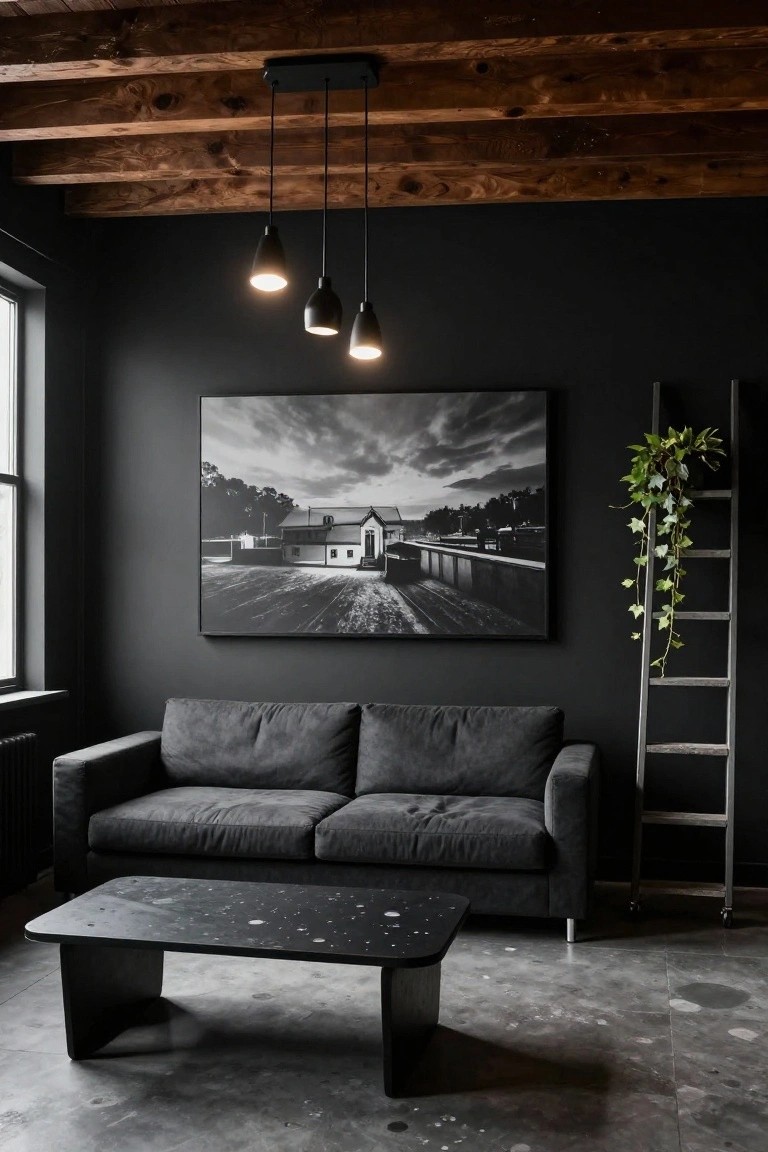 Dark living room with charcoal gray walls, exposed wooden ceiling beams, three black pendant lights, large black-and-white framed landscape photo, gray L-shaped sofa, black coffee table with white flecks, ivy plant on wooden ladder shelf, and concrete floor.