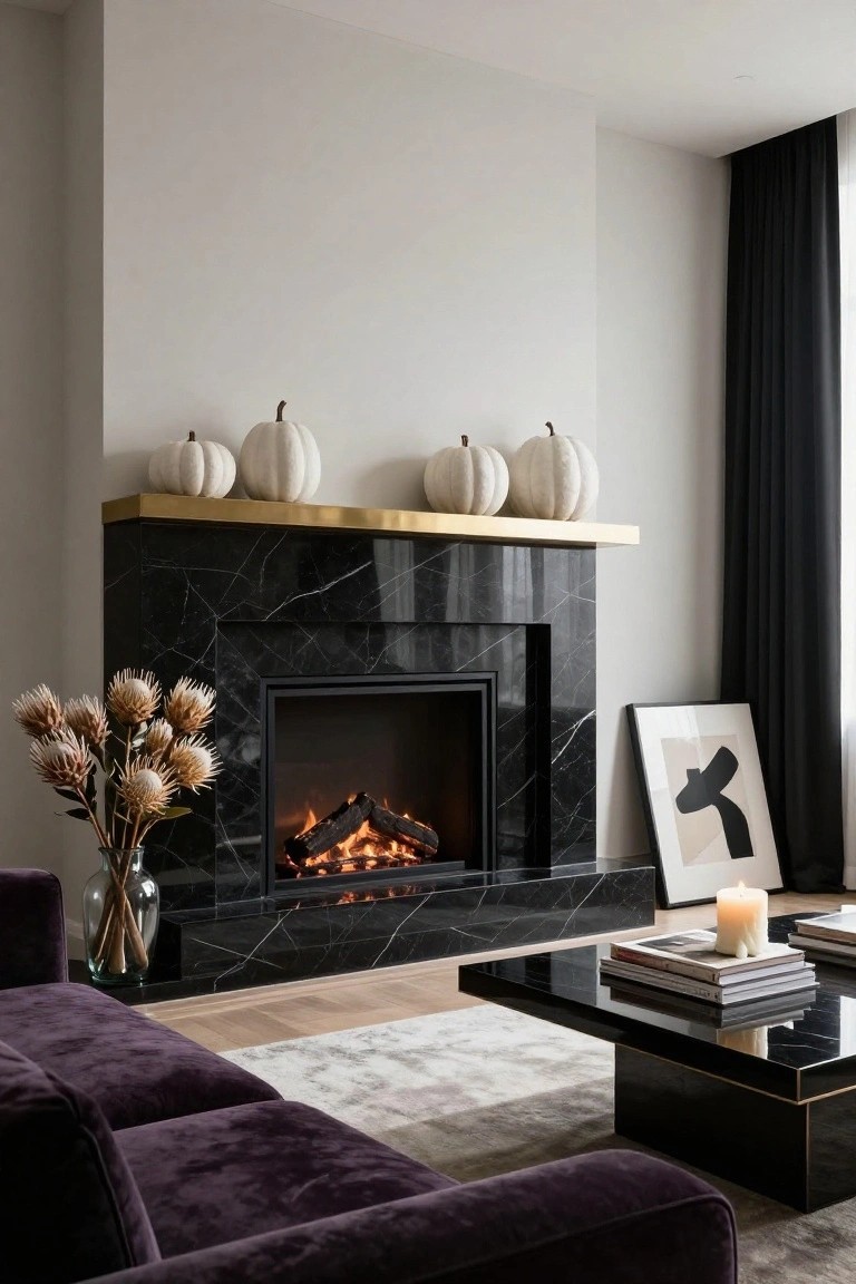 Modern living room interior with black marble fireplace, gold-trimmed mantel holding several white pumpkins, purple velvet sofa, black coffee table with stacked books and white candle, and abstract framed artwork leaning on the floor.