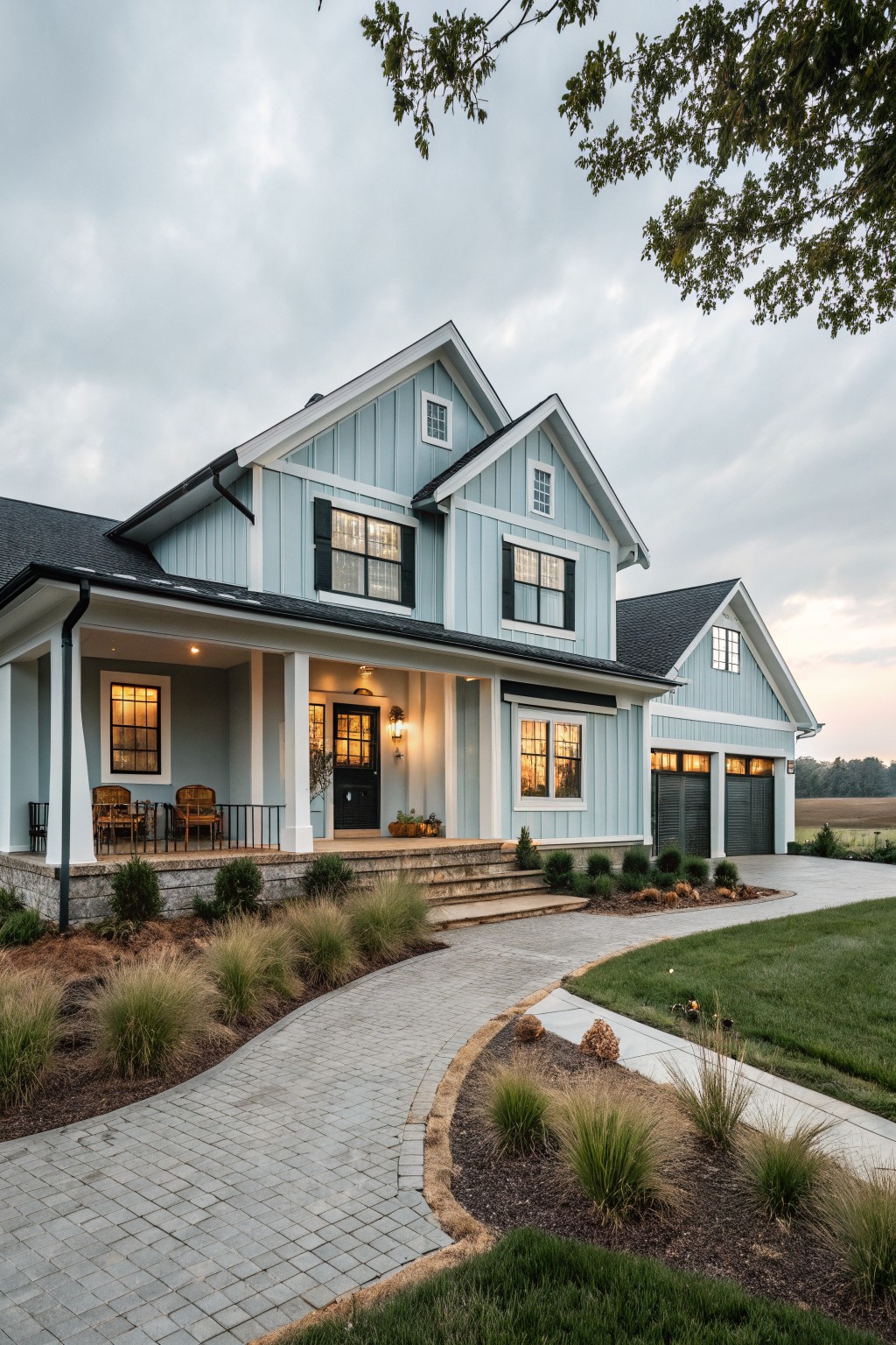 A two-story modern farmhouse with light blue horizontal siding, black shutters and trim, covered front porch with columns, attached garage, brick walkway, and ornamental grasses along the yard edge.