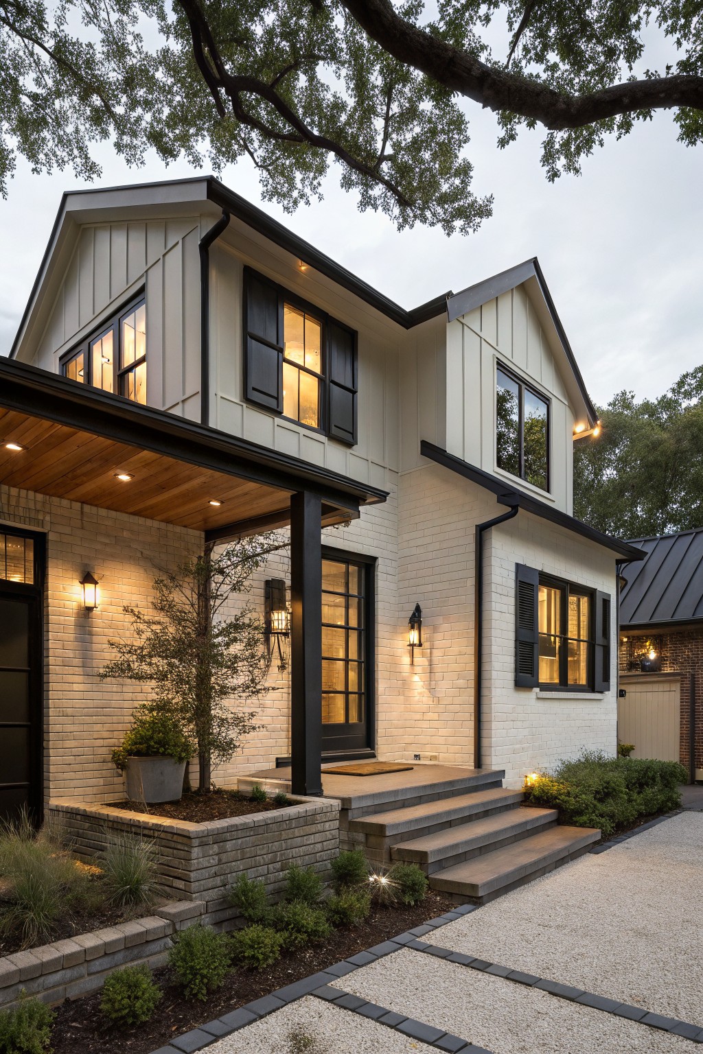 Modern farmhouse house exterior with light shiplap siding, white brick base, black window frames and door, covered porch with wood ceiling and metal posts, steps to entry, low plantings, and gravel path.
