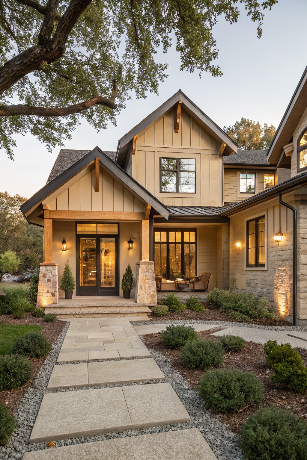 Beige board-and-batten sided modern farmhouse ranch house exterior featuring a covered entry porch with wood beams, stone pillars, lanterns, potted plants, and a stone pathway edged by shrubs and gravel.