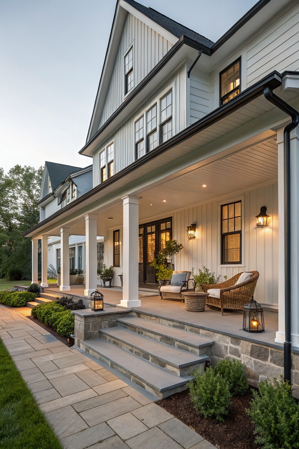 White farmhouse with stone porch, wicker chairs, and lantern-lit steps.