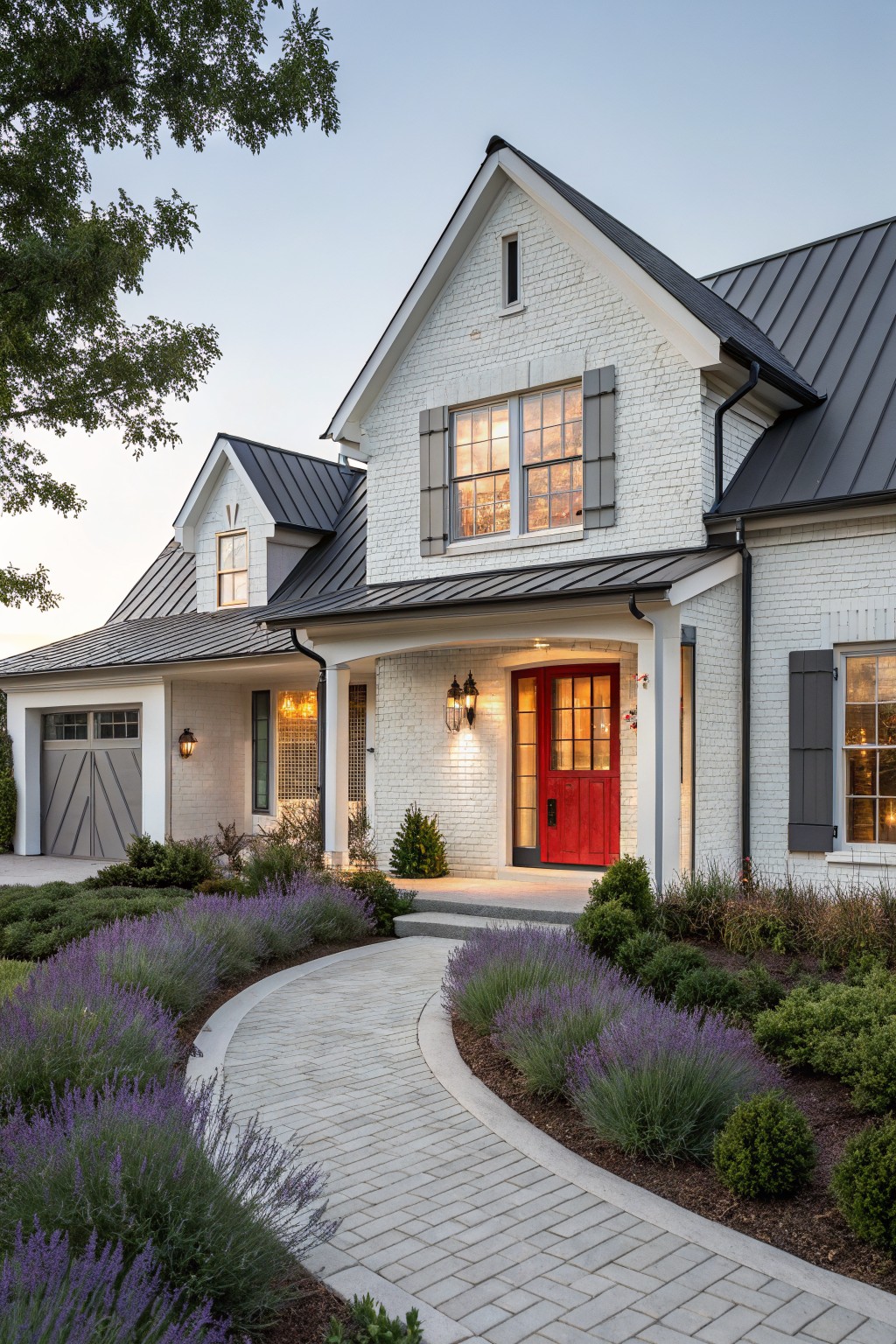 White brick rustic modern farmhouse with black metal roof, red double front door under covered porch, gray garage door, and curved gray paver path edged with lavender plants and shrubs.
