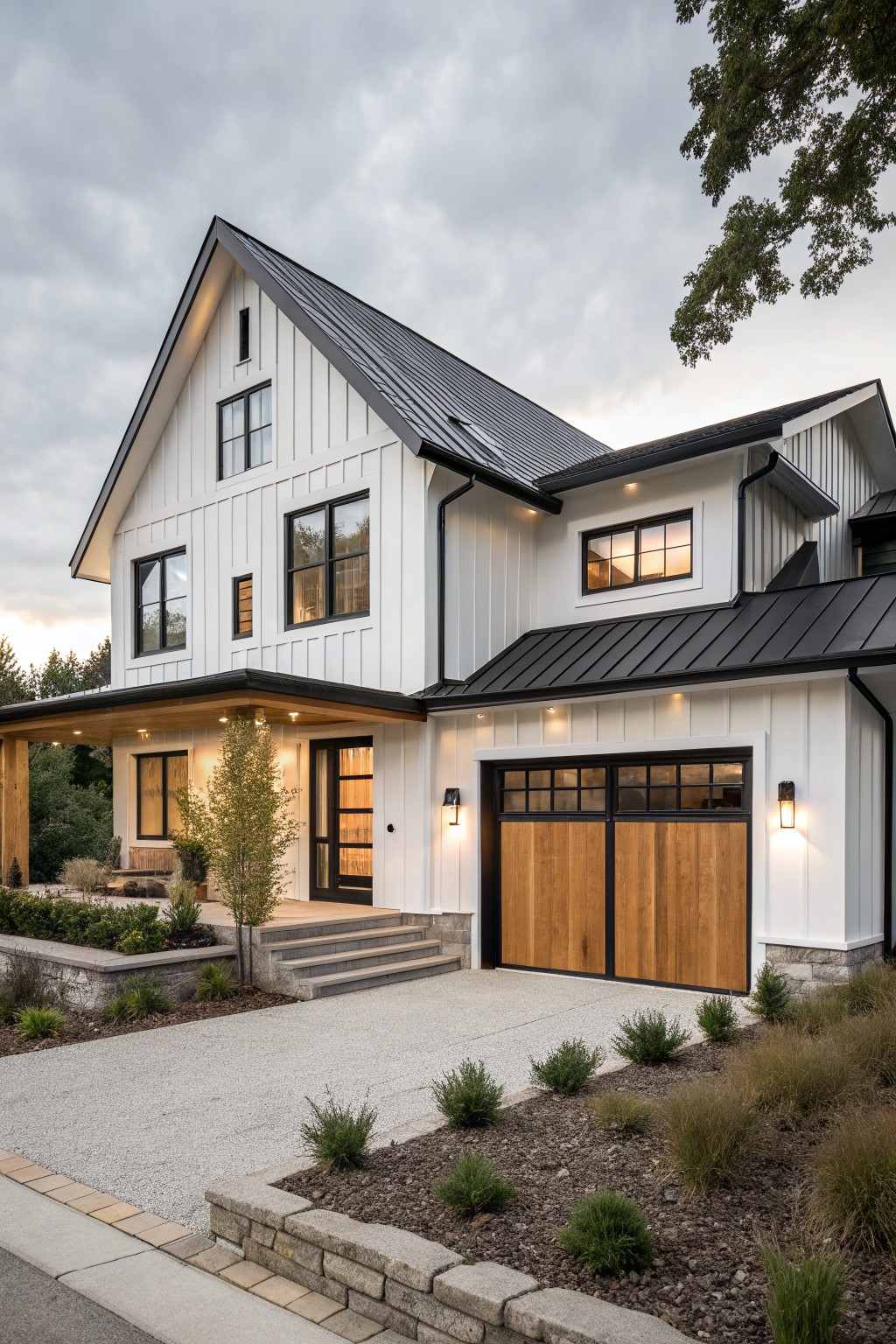 White board and batten sided modern farmhouse exterior featuring a black standing seam metal roof, attached garage with wooden doors, covered wooden porch entry, gravel driveway, low plantings, and stone retaining walls under a cloudy sky.
