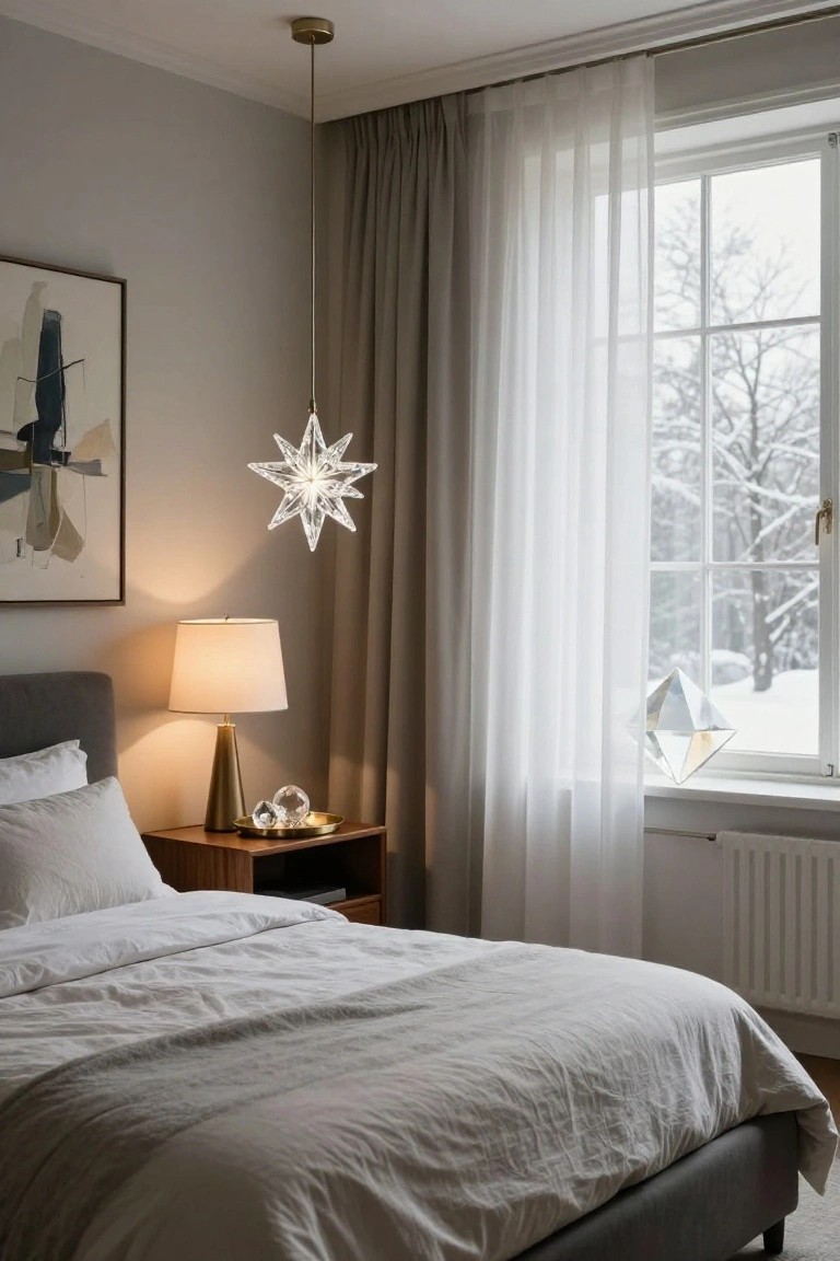 Gray bedroom with upholstered bed, wooden nightstand holding gold lamp and crystal spheres on tray, crystal star pendant light hanging from ceiling, sheer curtains at window with snowy view and crystal pyramid on sill.