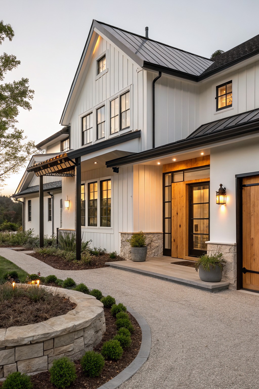 Exterior of a two-story modern farmhouse featuring white board-and-batten siding, black standing-seam metal roof, wooden pivot entry door with glass sidelights under a covered porch, gravel driveway, and low landscaping with stone retaining wall.