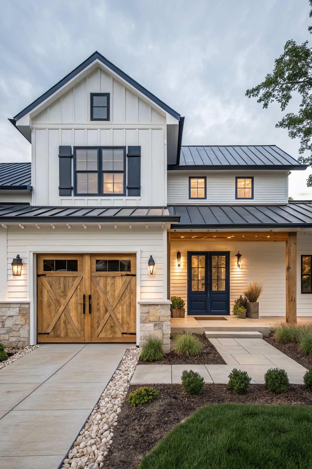 White modern farmhouse house exterior with navy blue double front doors, wooden double garage doors, black metal roof, stone accents, lanterns, potted plants, and landscaped front yard with concrete walkway and gravel edging.