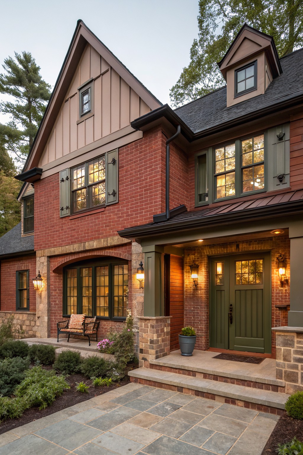 Front exterior of a two-story house with red brick lower walls and light vertical siding on upper levels, featuring a covered porch with green double doors, lanterns, a bench, stone accents, and surrounding landscaping with plants and a stone pathway.