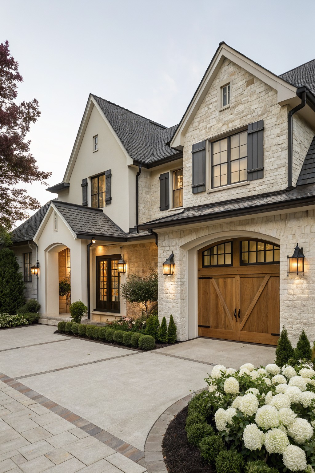 Elegant stone-and-stucco house with arched wooden garage and white flowers.
