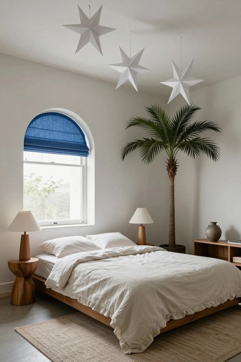 Minimalist bedroom featuring a low wooden platform bed with white linens, two wooden side tables with lamps, a tall potted palm tree, an arched window with blue roman shade, and several white paper star decorations hanging from the ceiling.