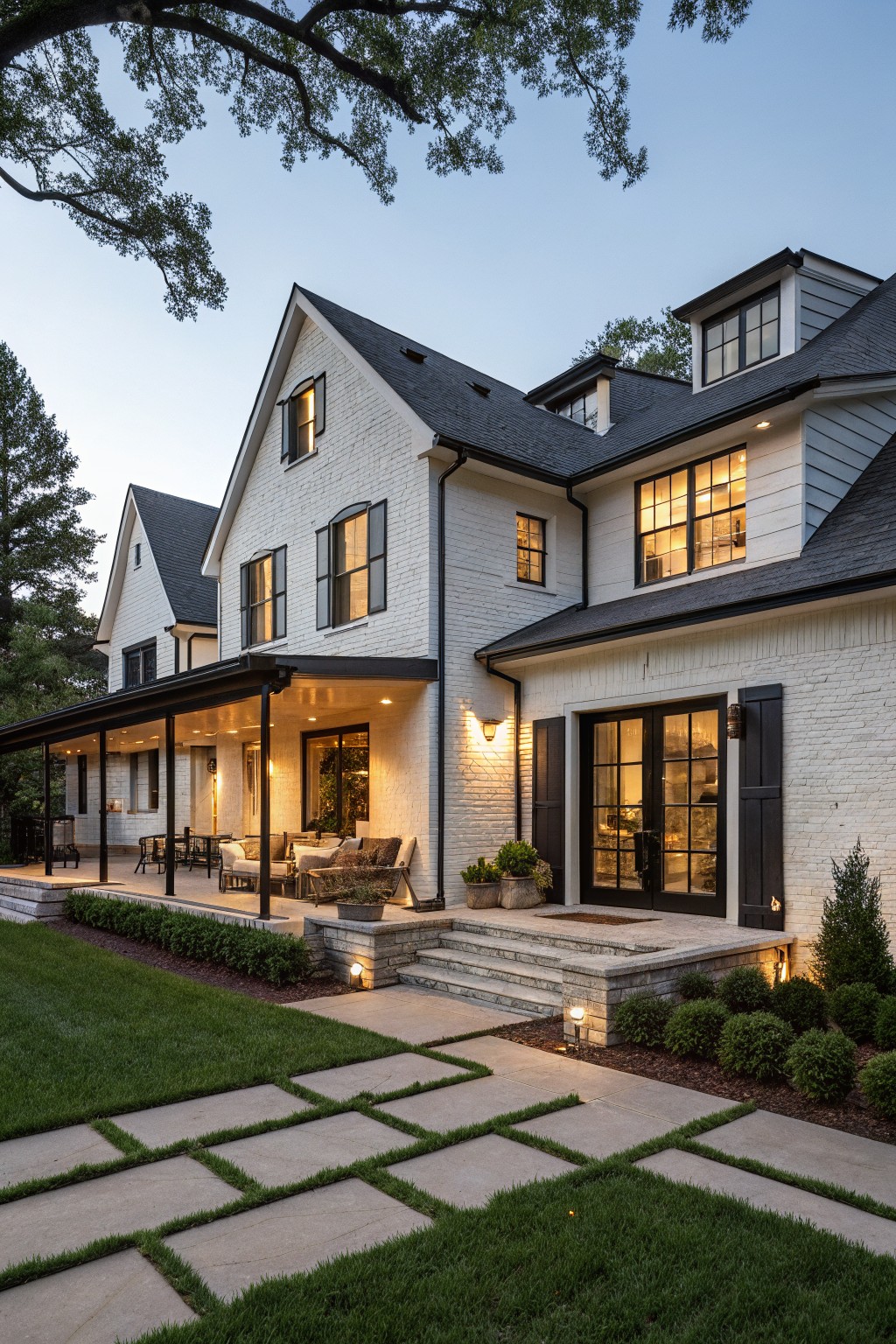 White brick modern farmhouse house exterior at dusk with black shutters, trim, windows, covered porch, stone entry steps, and grass pathway.