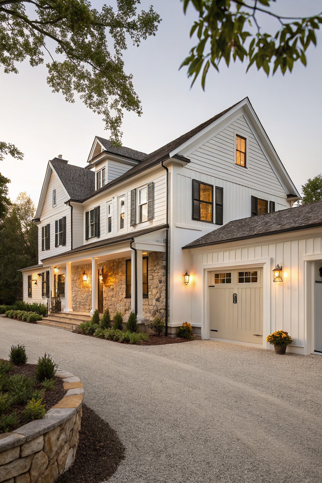 White board and batten farmhouse exterior with gabled roof, covered front porch on stone base, attached garage, lanterns, gravel driveway, and low landscaping.