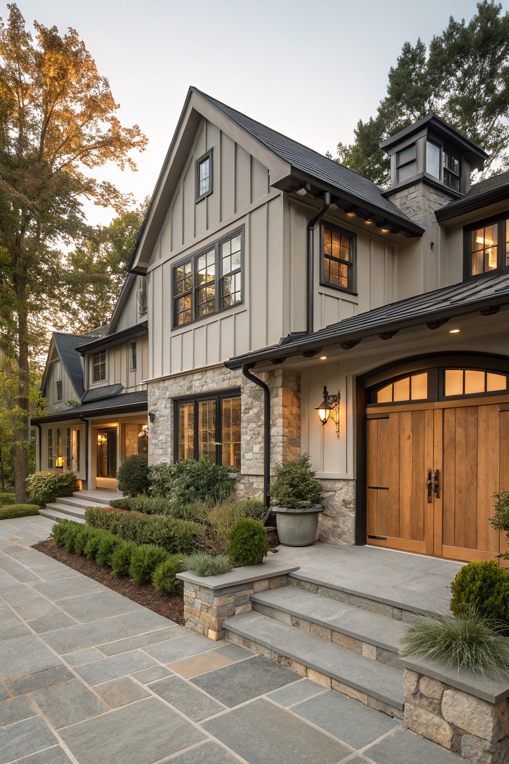 A two-story modern farmhouse exterior with greige board-and-batten siding, black metal roof and trim, stone base, wooden arched garage doors, and landscaping along a stone paver walkway.