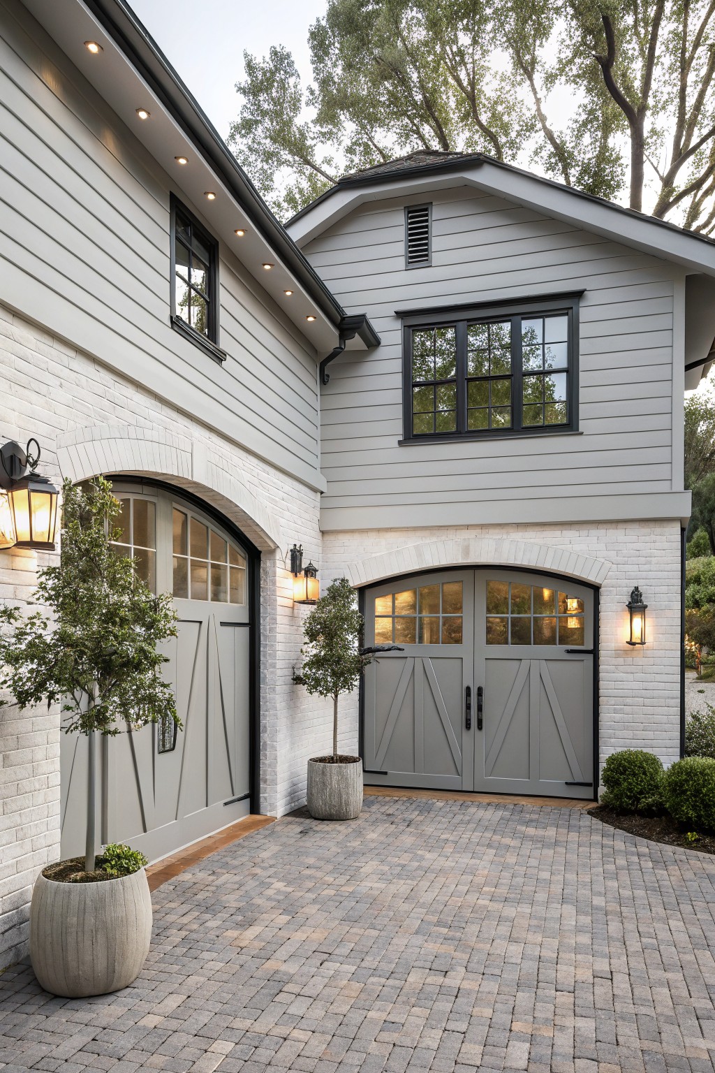 Modern two-story home with arched gray garage doors and potted trees.