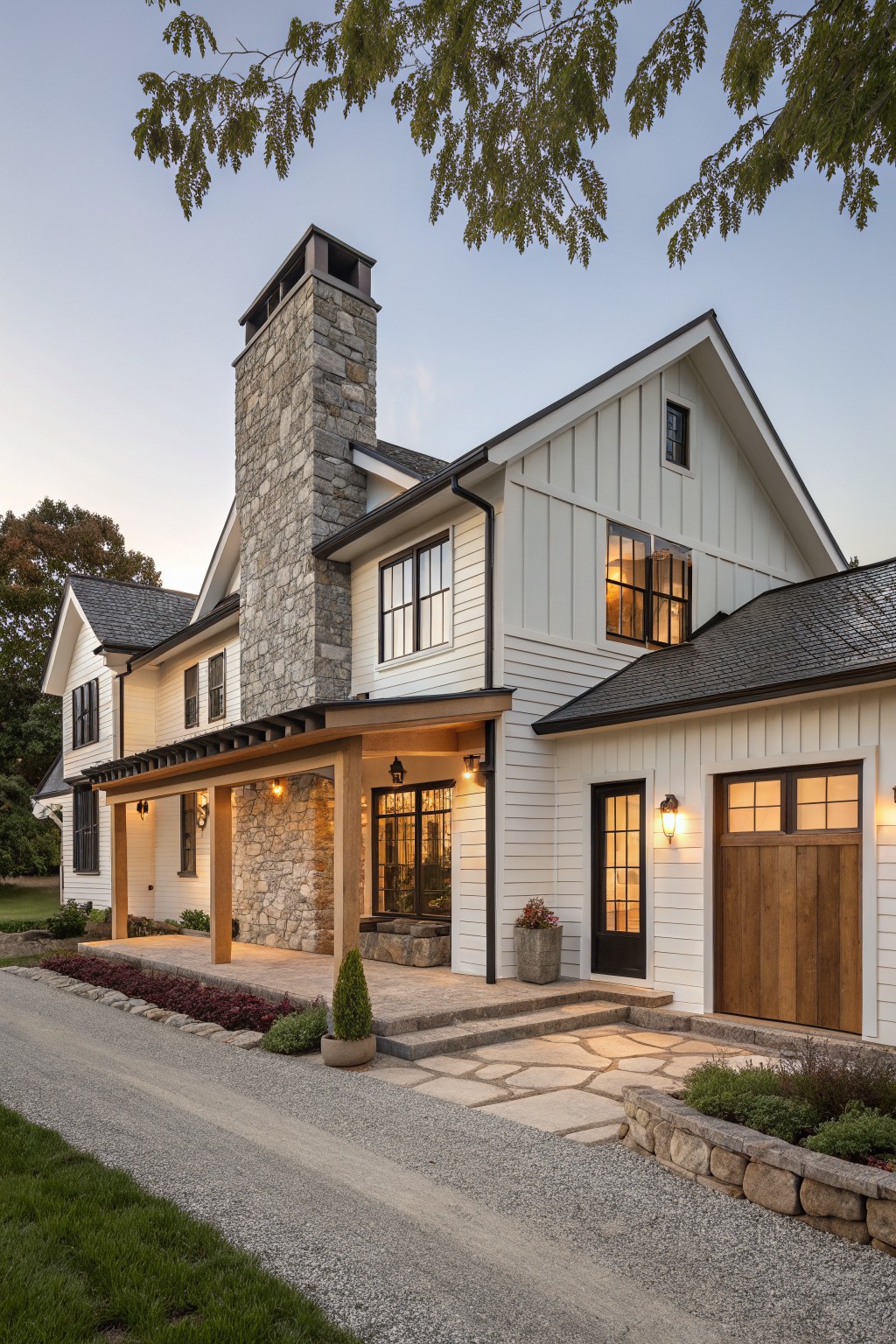 One-story modern farmhouse exterior with tall gray stone chimney, white board-and-batten siding, covered porch supported by stone columns, attached garage with wood doors, gravel driveway, stone steps, and low landscaping.