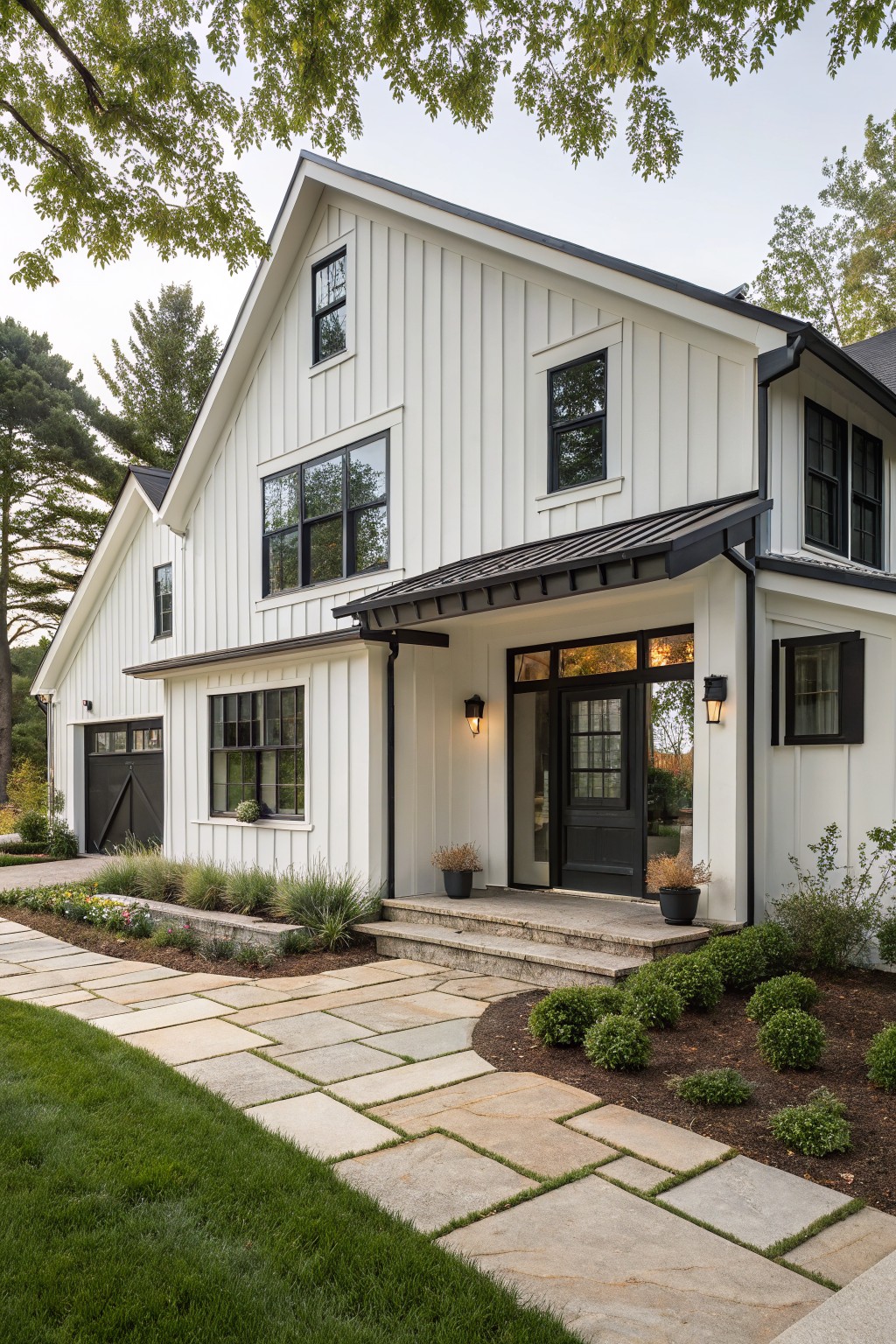 White board-and-batten sided modern farmhouse house with black trim on windows and doors, black metal porch roof over glass entry door, black garage door, stone entry steps, and low landscaping along a flagstone path.